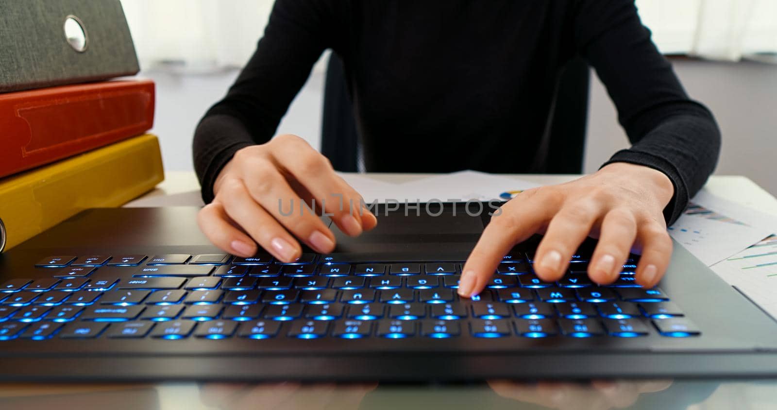 Female hands typing on laptop while sitting at office desk indoors. Woman fingers typing and texting on computer keyboard while working online, writes mails.