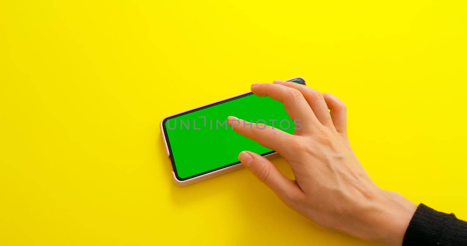 Green screen chroma key phone. Female hand doing gestures for touch screen. Phone green screen for product placement. Yellow background.