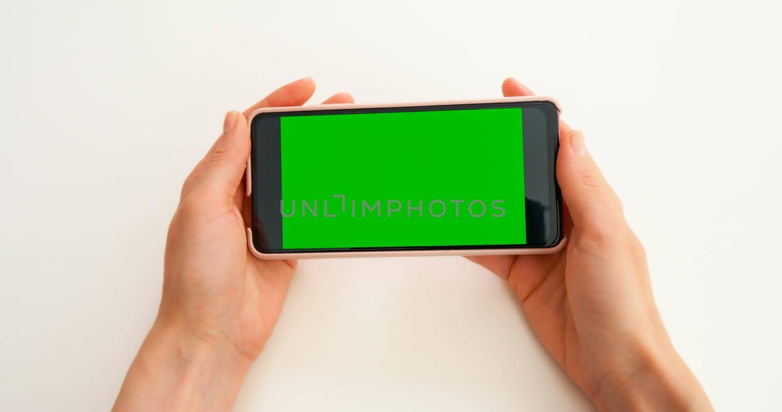 Green Screen Mock-up Chroma Key smartphone. Watching photo content, blogs, POV. Close-Up of Woman Hands are holding horizontal smartphone with Green Screen on yellow background.