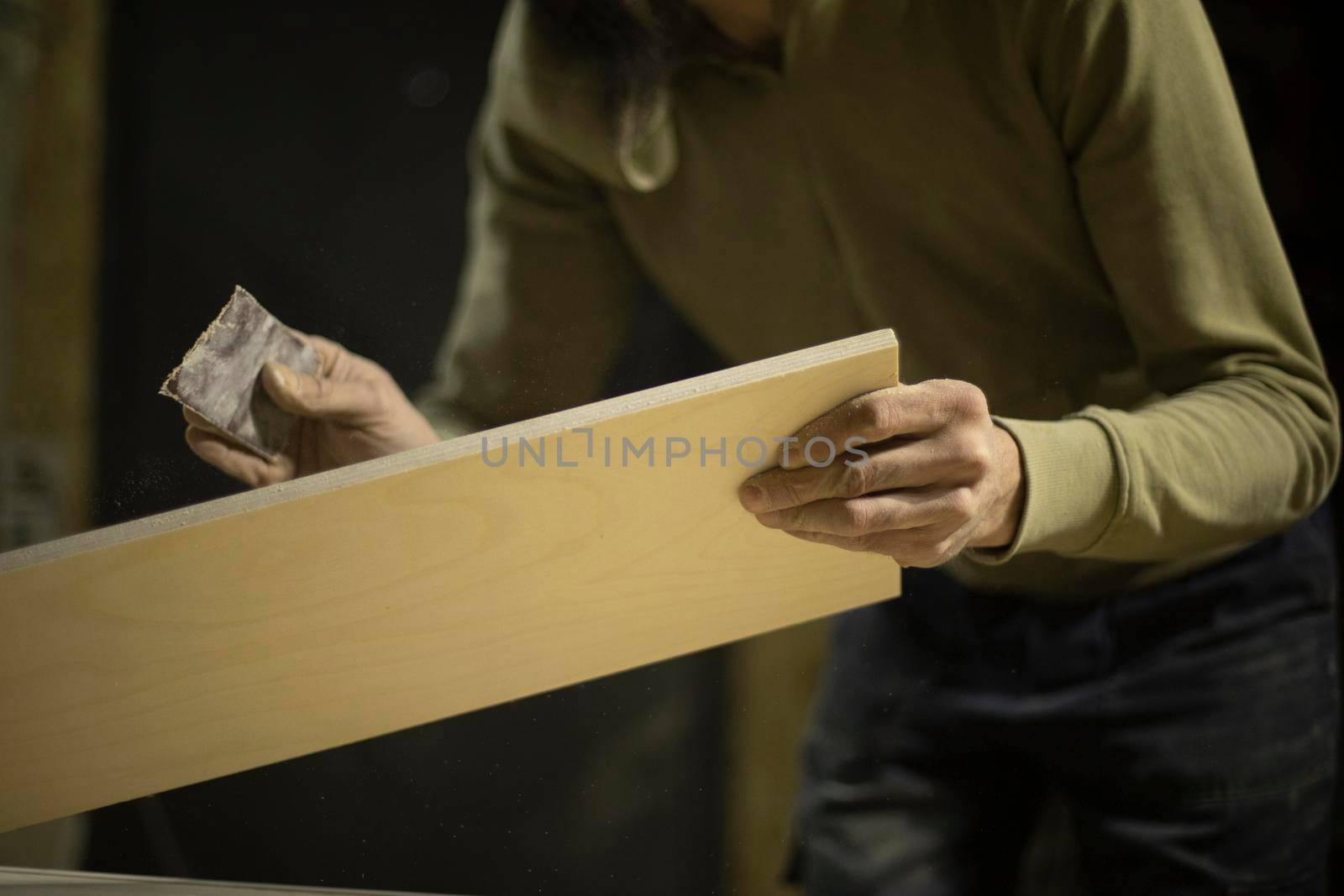 Carpenter grinds board. Man creates furniture. Hands hold sanding paper. Worker processes wood.