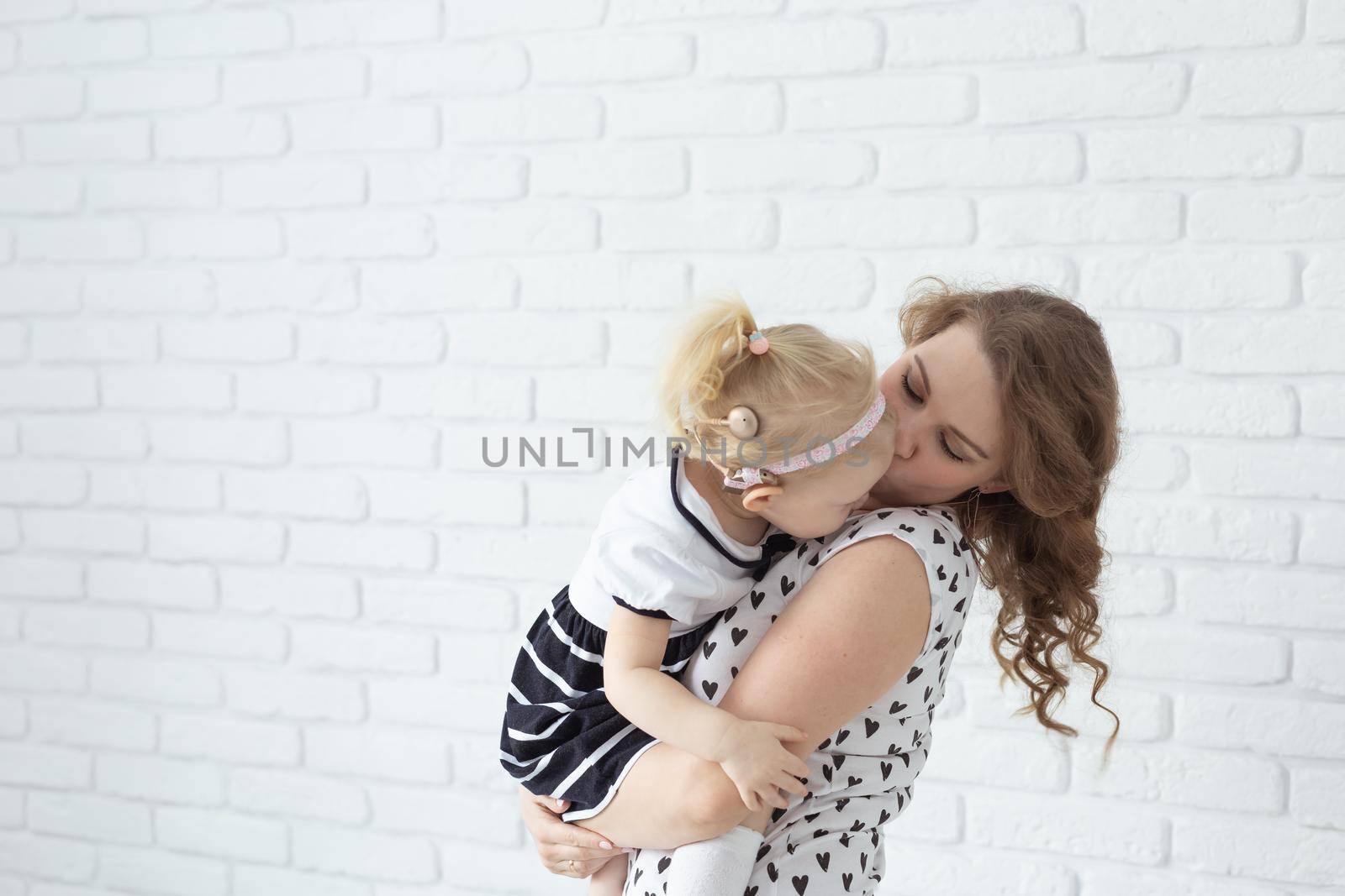 Mother holds and having fun her child with hearing aids and cochlear implants on white brick wall with copy space and place for advertising . Deaf and innovating medicine technologies concept by Satura86