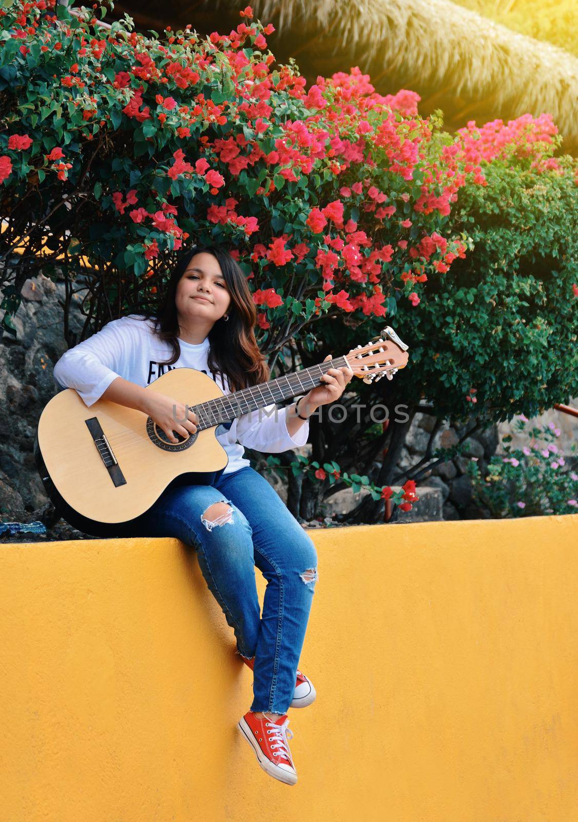 A girl sitting playing guitar outdoors, Portrait of a smiling girl playing guitar, Lifestyle of a girl playing guitar outdoors