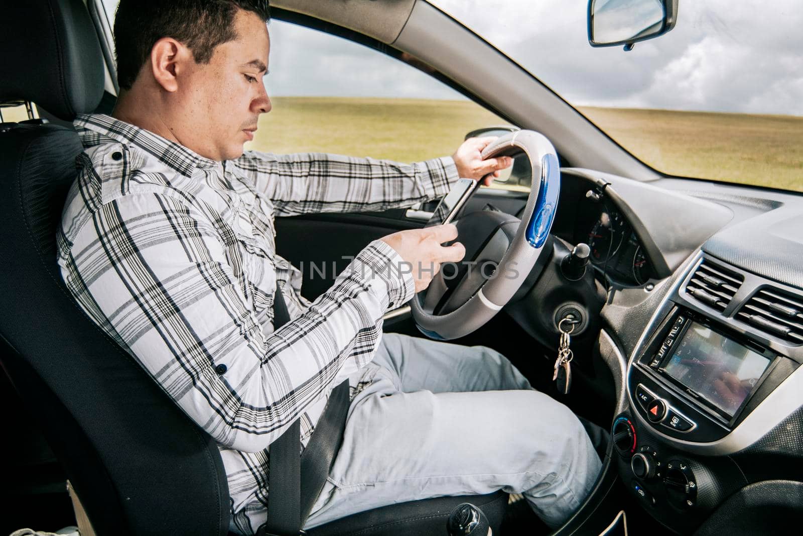 Man sitting in his car texting with his cell phone, Side view of a young man sitting inside car using mobile phone, Young man sitting in a car and looking at a mobile phone