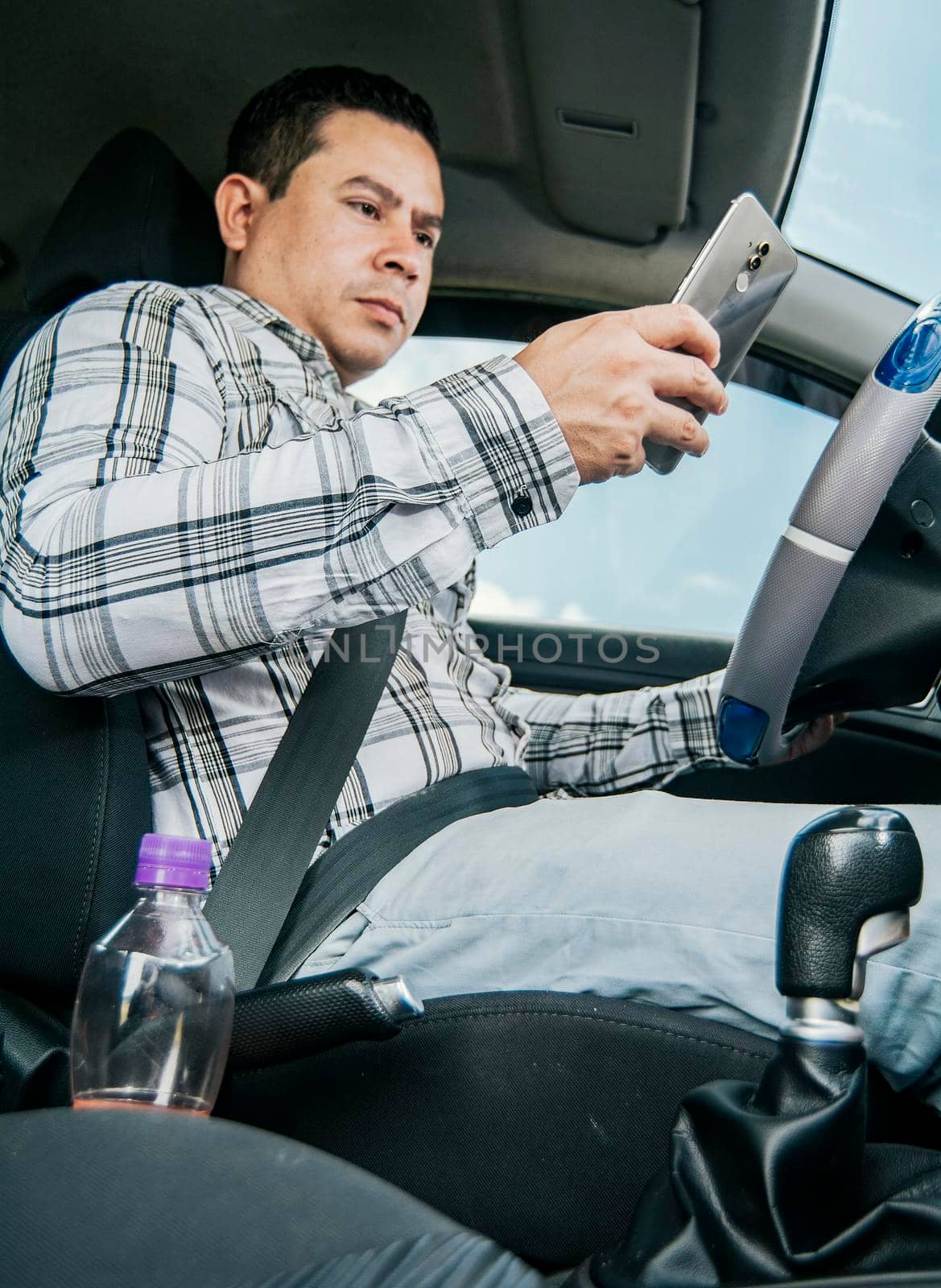 Man sitting in his car texting with his cell phone, Side view of a young man sitting inside car using mobile phone, Young man sitting in a car and looking at a mobile phone