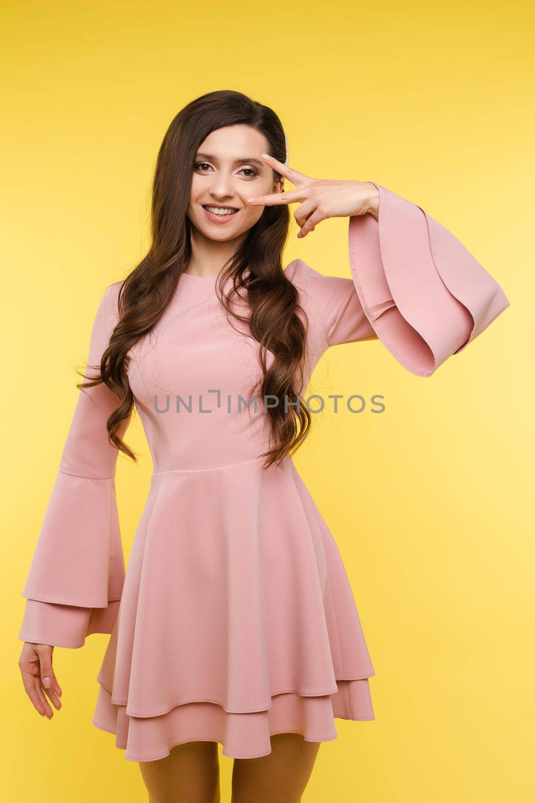 Side view of brunette girl with long hair posing at camera. Young beautiful girl in pink dress lightly leaning forward and flirting. Pretty glamour lady sending in elegant and stylish look air kisses.
