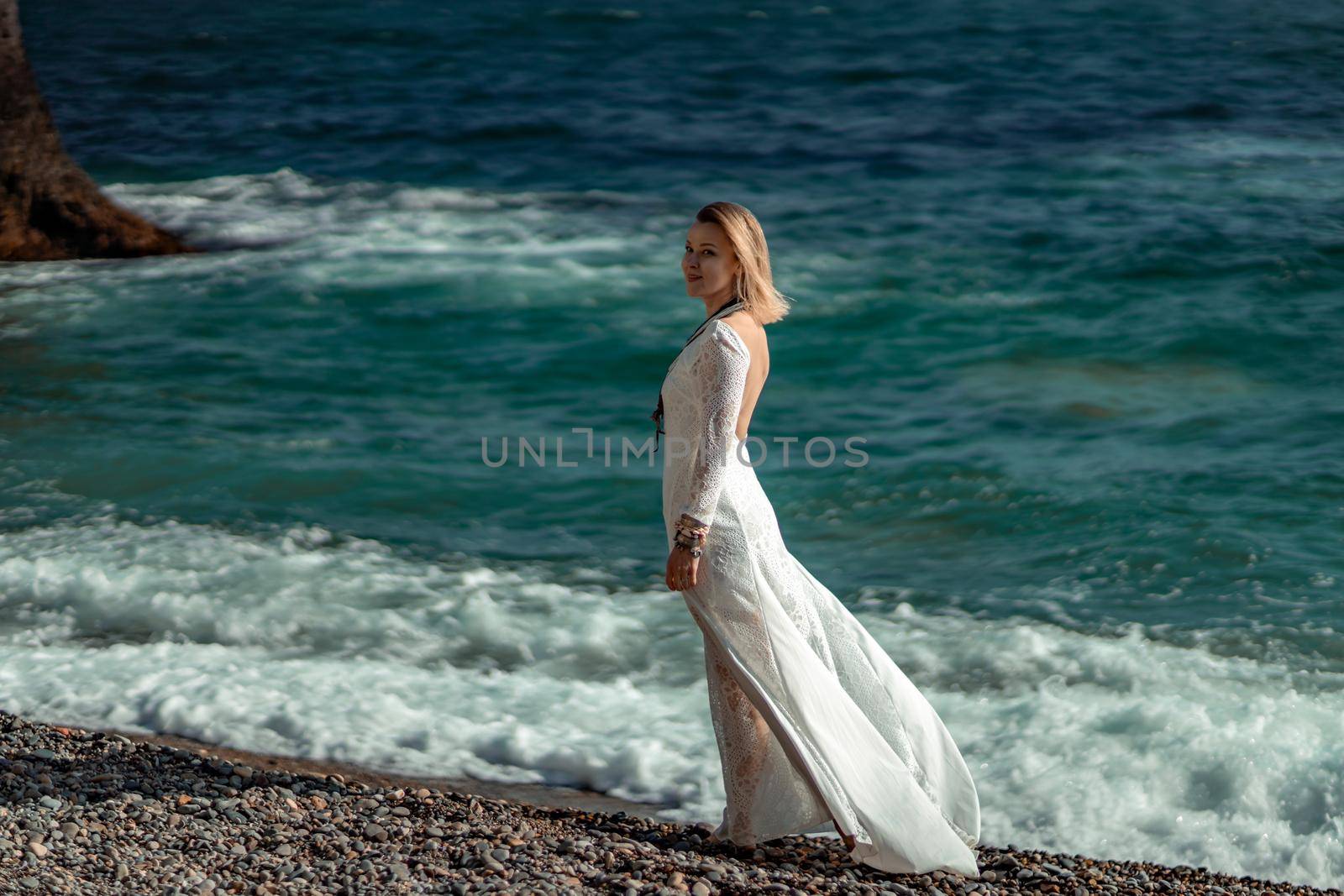 Middle aged woman looks good with blond hair, boho style in white long dress on the beach decorations on her neck and arms. by Matiunina