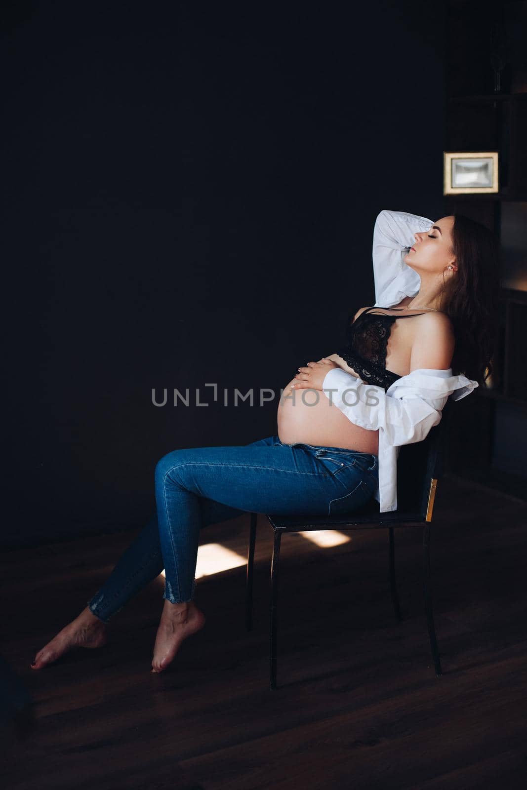 Side view of pregnant woman sitting in chair and posing by StudioLucky