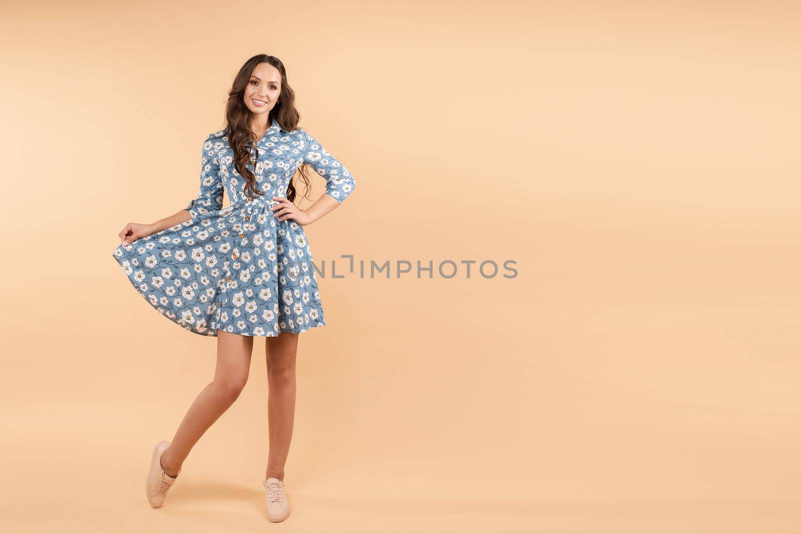 Pretty female in blue floral dress and sneakers smiling by StudioLucky