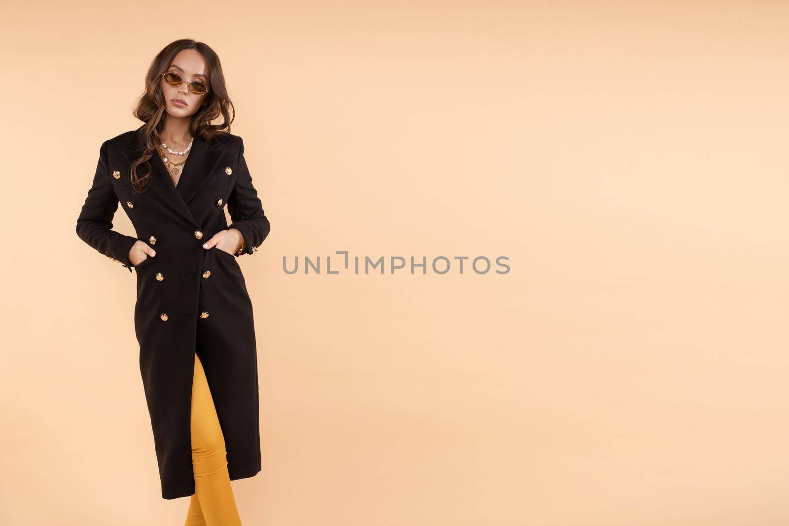 Serious business woman wearing black coat and glasses posing on isolated background. Sexy adorable lady going and looking at camera in studio. Concept of casual outfit and confidence.