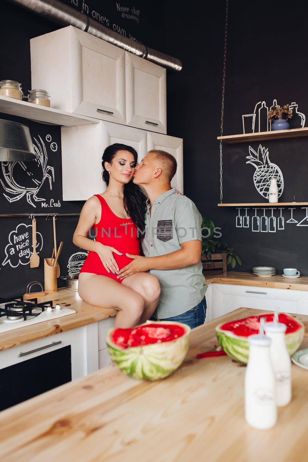 Lovely pair expecting little baby. Caring husband kissing beautiful pregnant wife while cooking dinner at kitchen. Future parents touching belly and hugging each other. Concept of pregnancy.