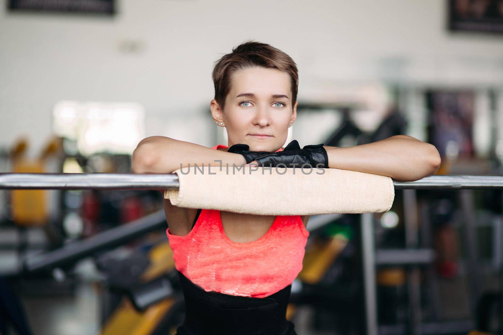 Woman with short hair in pink wear resting in gym after workout with barbell. by StudioLucky