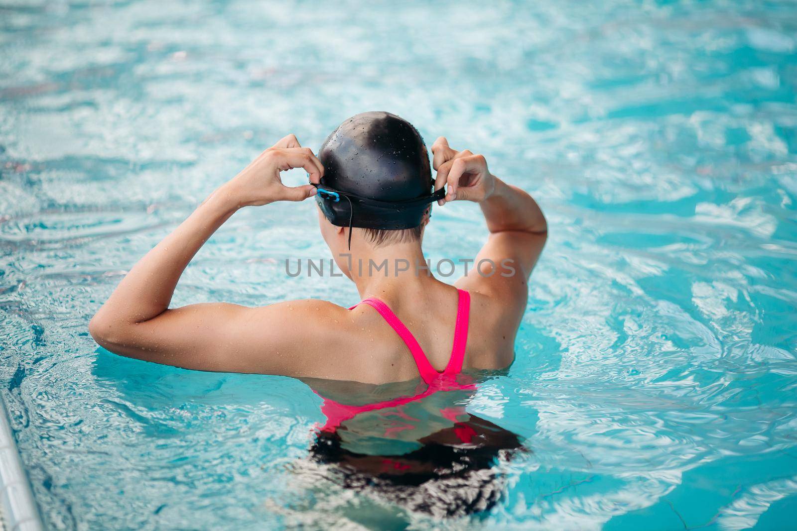 Sporty woman in cap swimming in the blue water pool. Athletic girl concentrated swimming, wearing in pink swimsuit, engaged in sports. Concept of water sport.