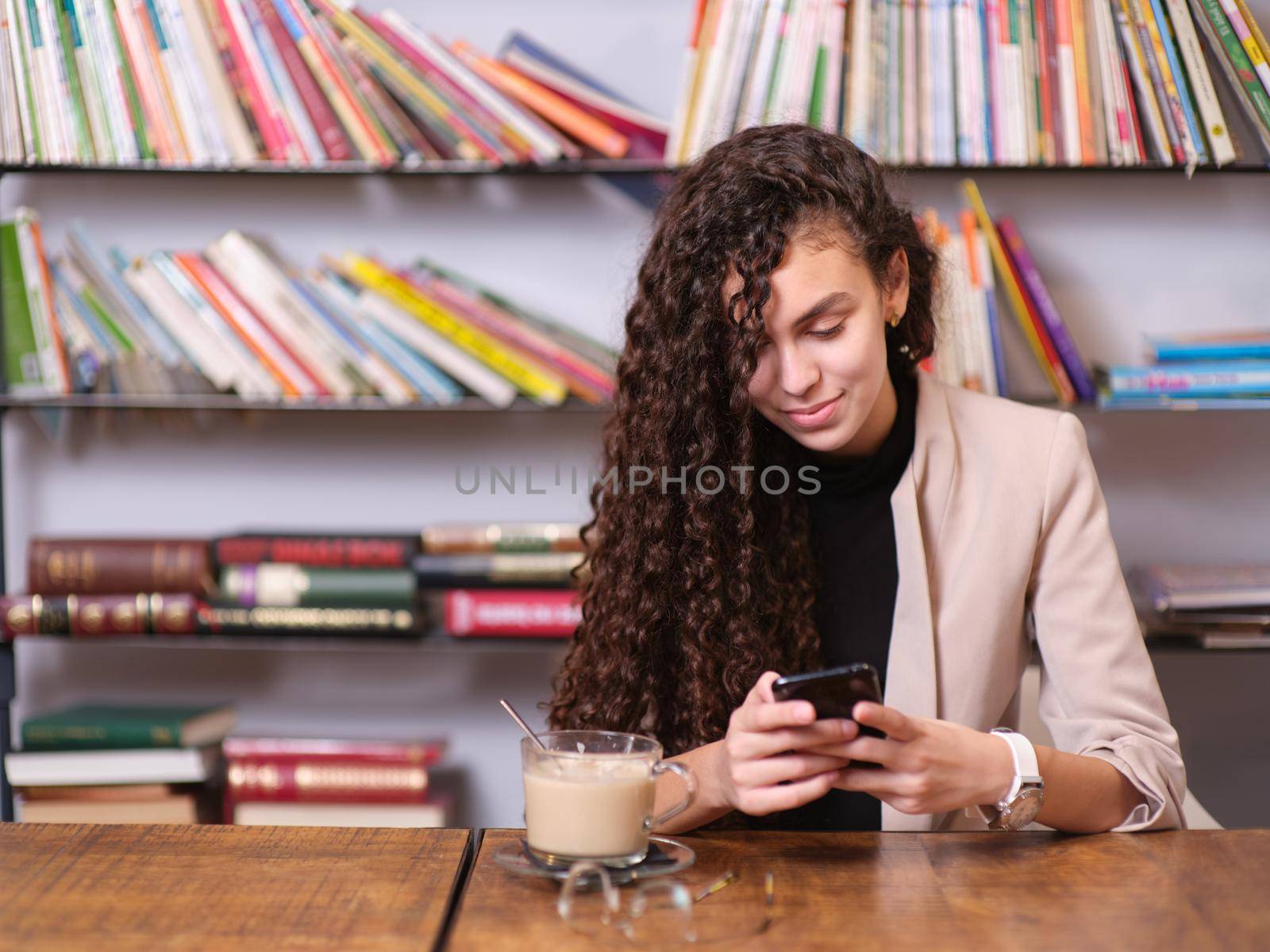 young woman checking her mobile phone while sitting with a hot drink by WesternExoticStockers