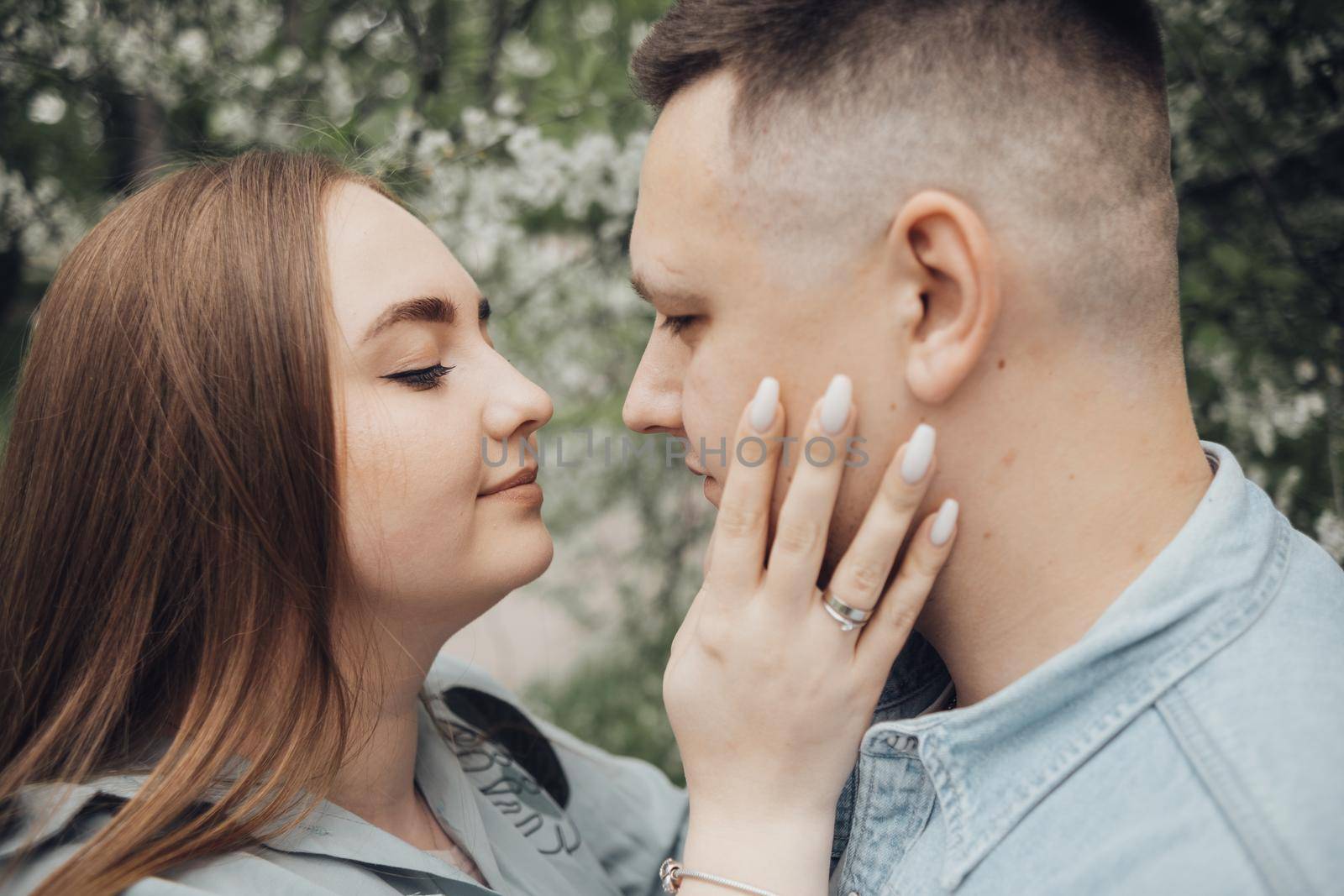 a guy and a girl stand against the background of a flowering tree and are going to kiss by Symonenko