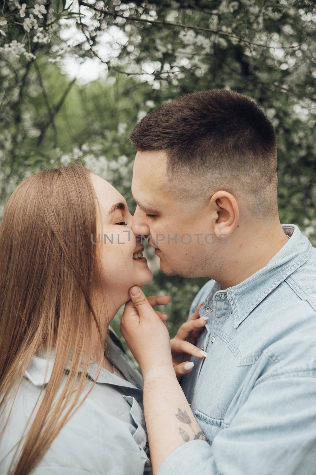 a guy and a girl stand against the background of a flowering tree and are going to kiss by Symonenko