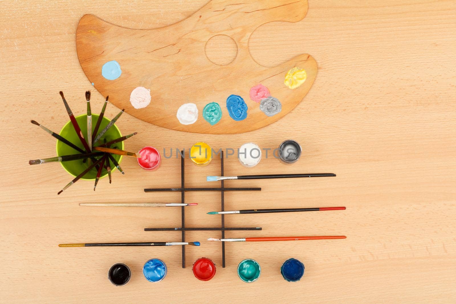 Wooden palette with paints and paintbrushes in a cup on wooden table Drawing set