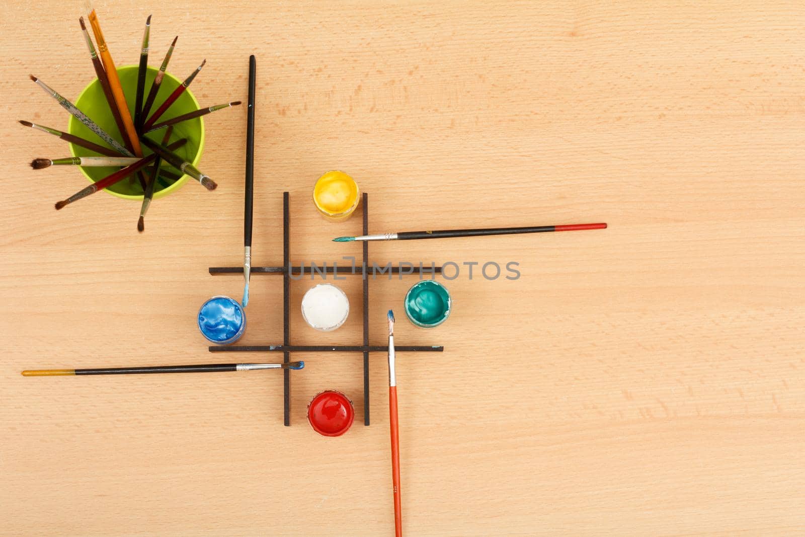 Paints and paintbrushes in a green cup on wooden background