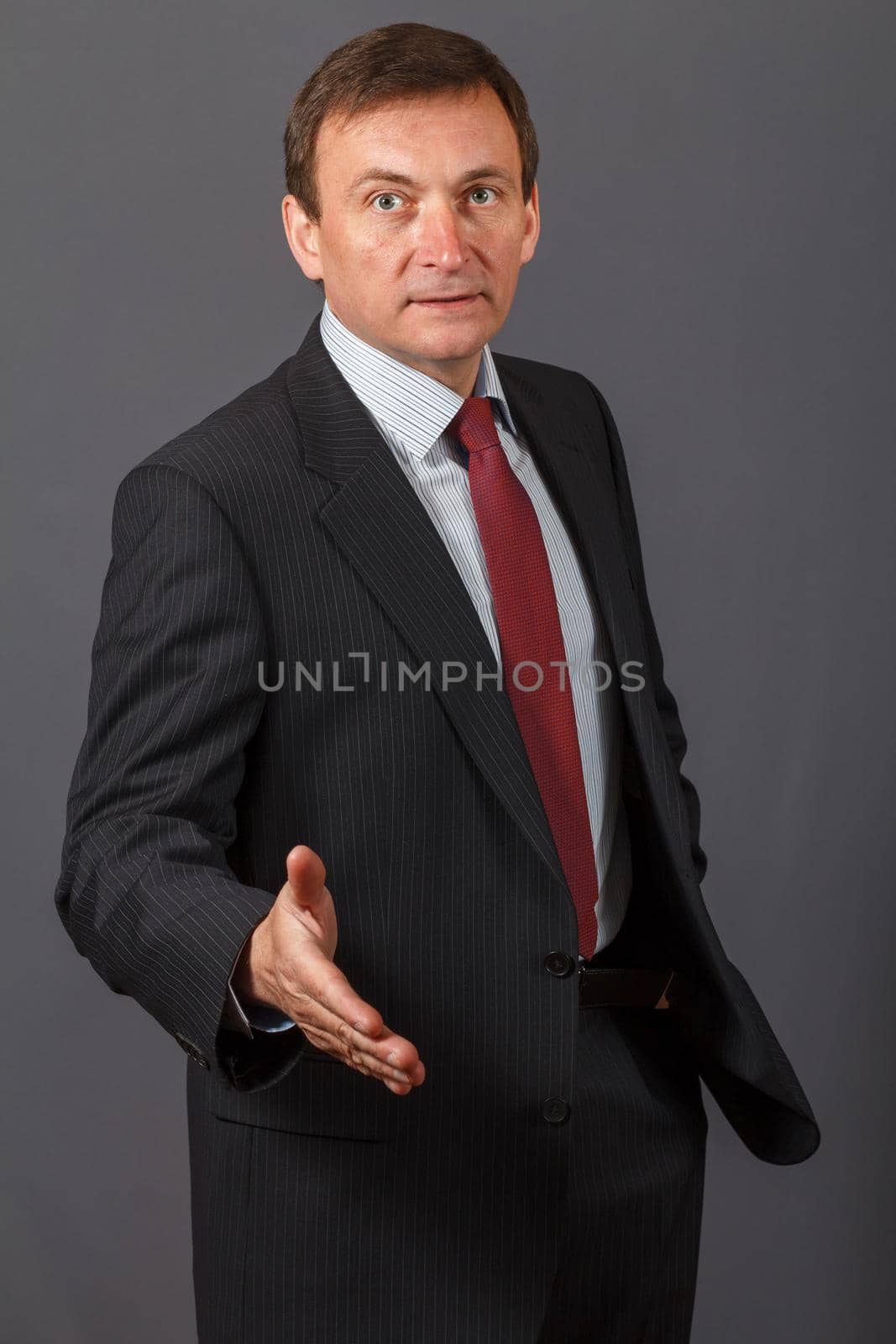 Confident and friendly elegant handsome mature businessman standing in front of a gray background in a studio giving a hand for greetings