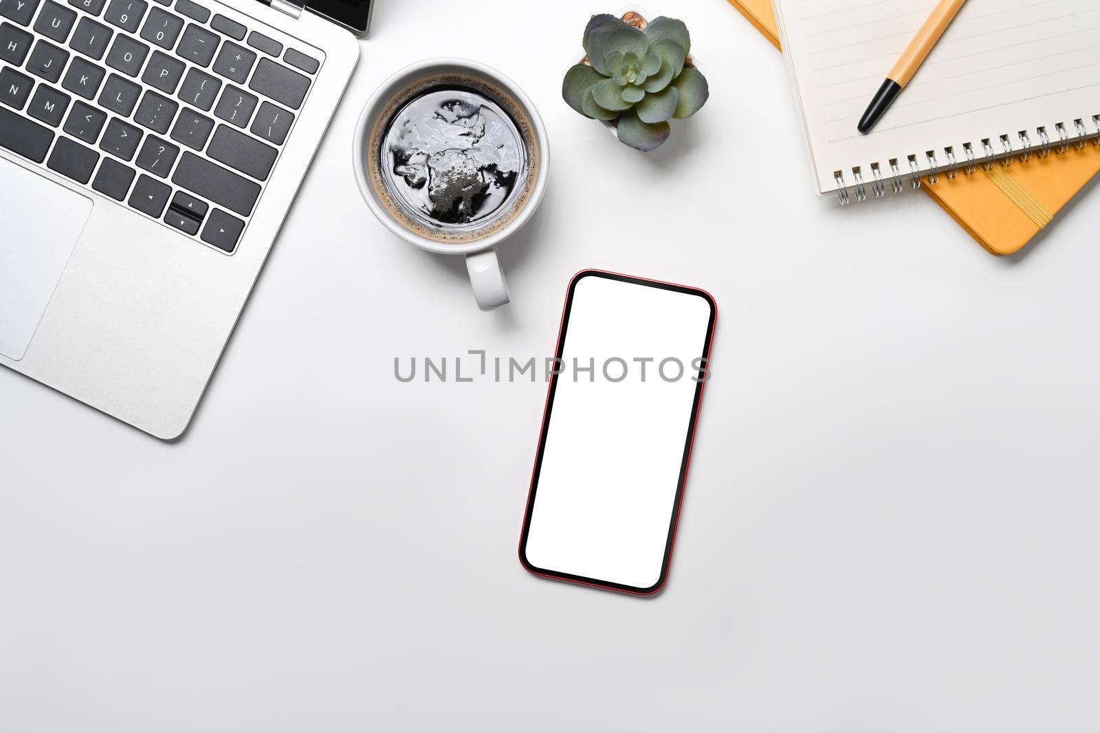 Mockup mobile phone with lank screen, laptop, coffee cup and notepad on white office desk.