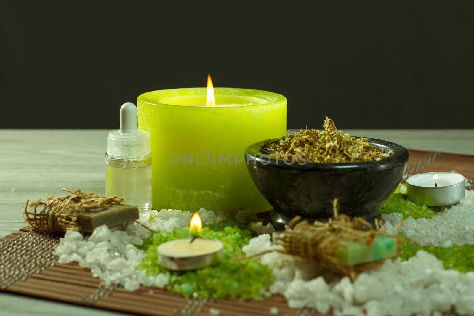 Spa accessories with soap, bowl with dried chamomile flowers, bottles with aromatic oil, sea salt, candles on bamboo napkin