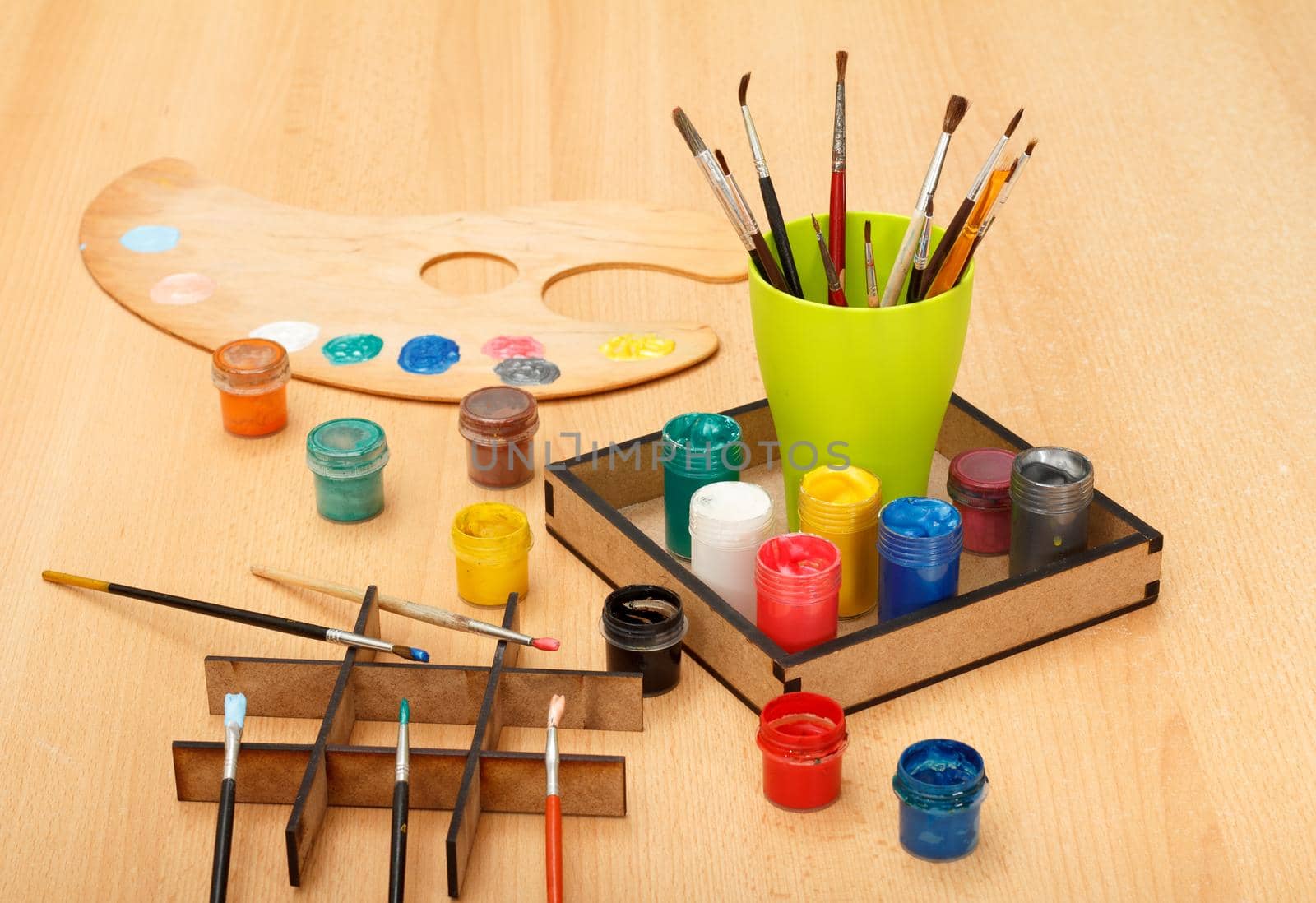 Wooden palette with colorful paints and cup with paintbrushes on the table