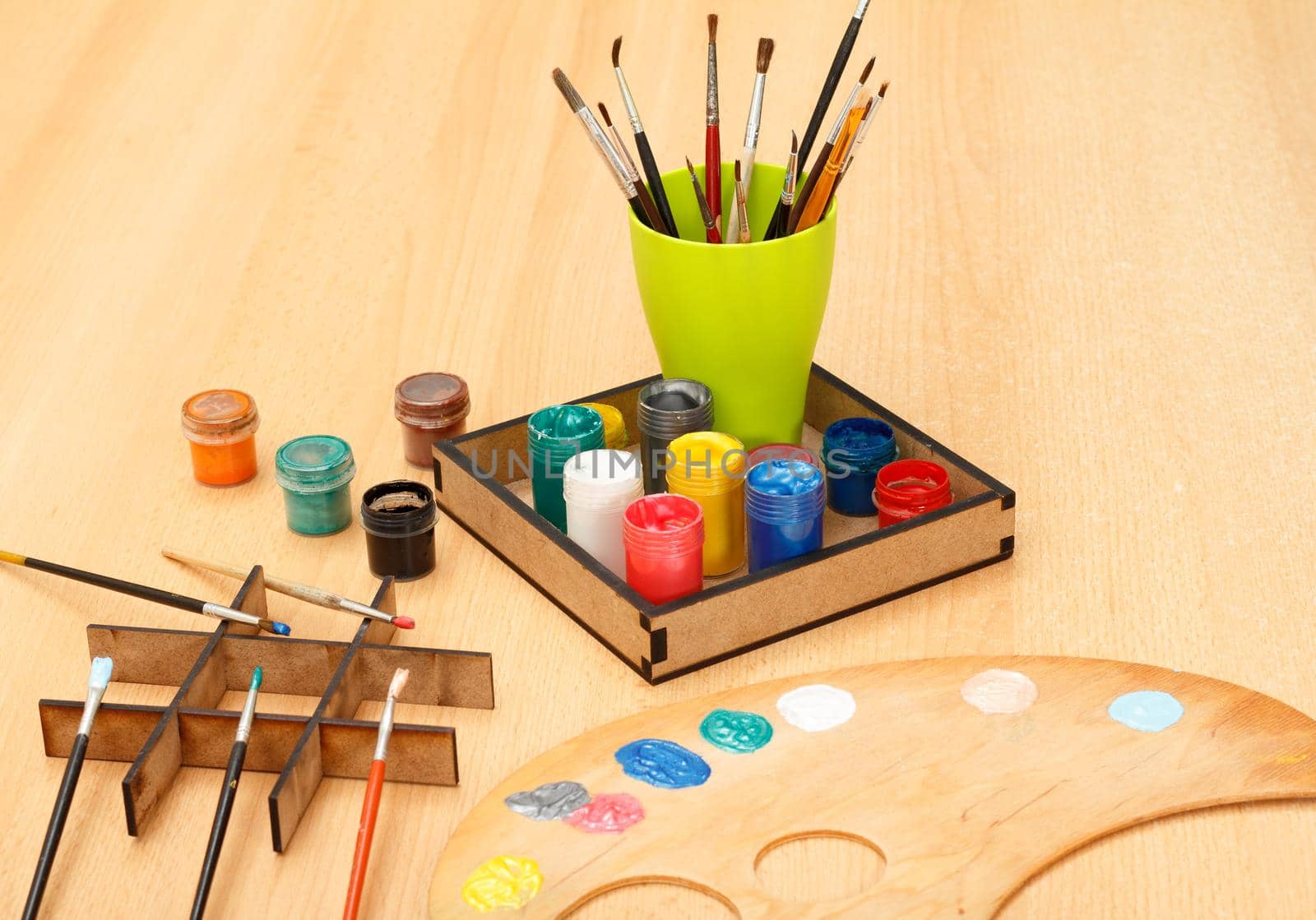 Wooden palette with laying on paints and cup with paintbrushes on the table