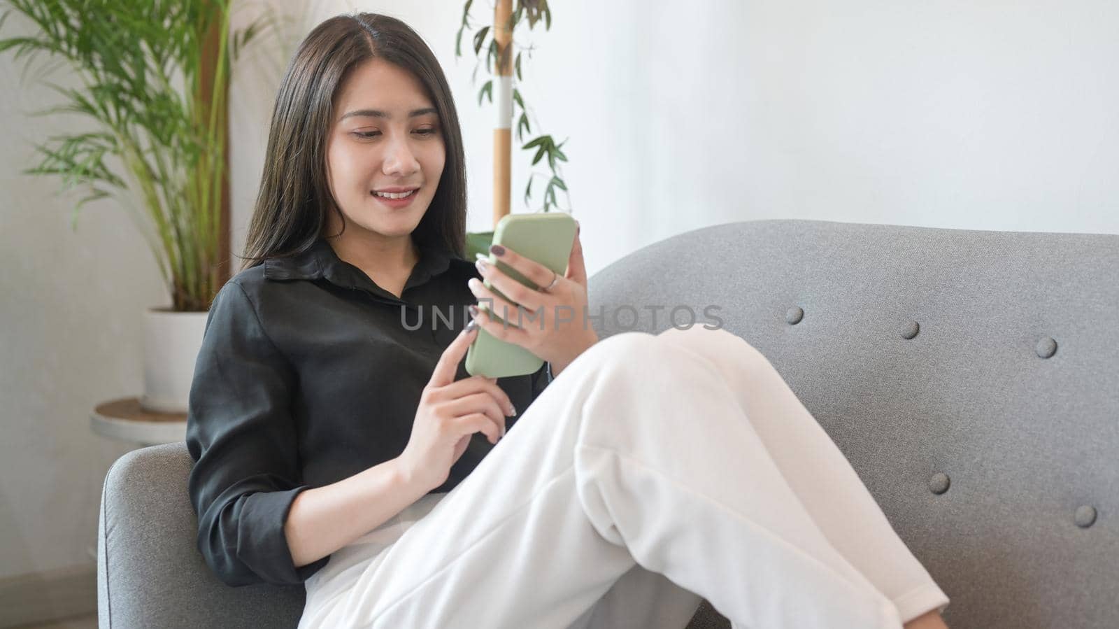 Young woman resting on sofa and using mobile phone for ordering delivery, checking social media.