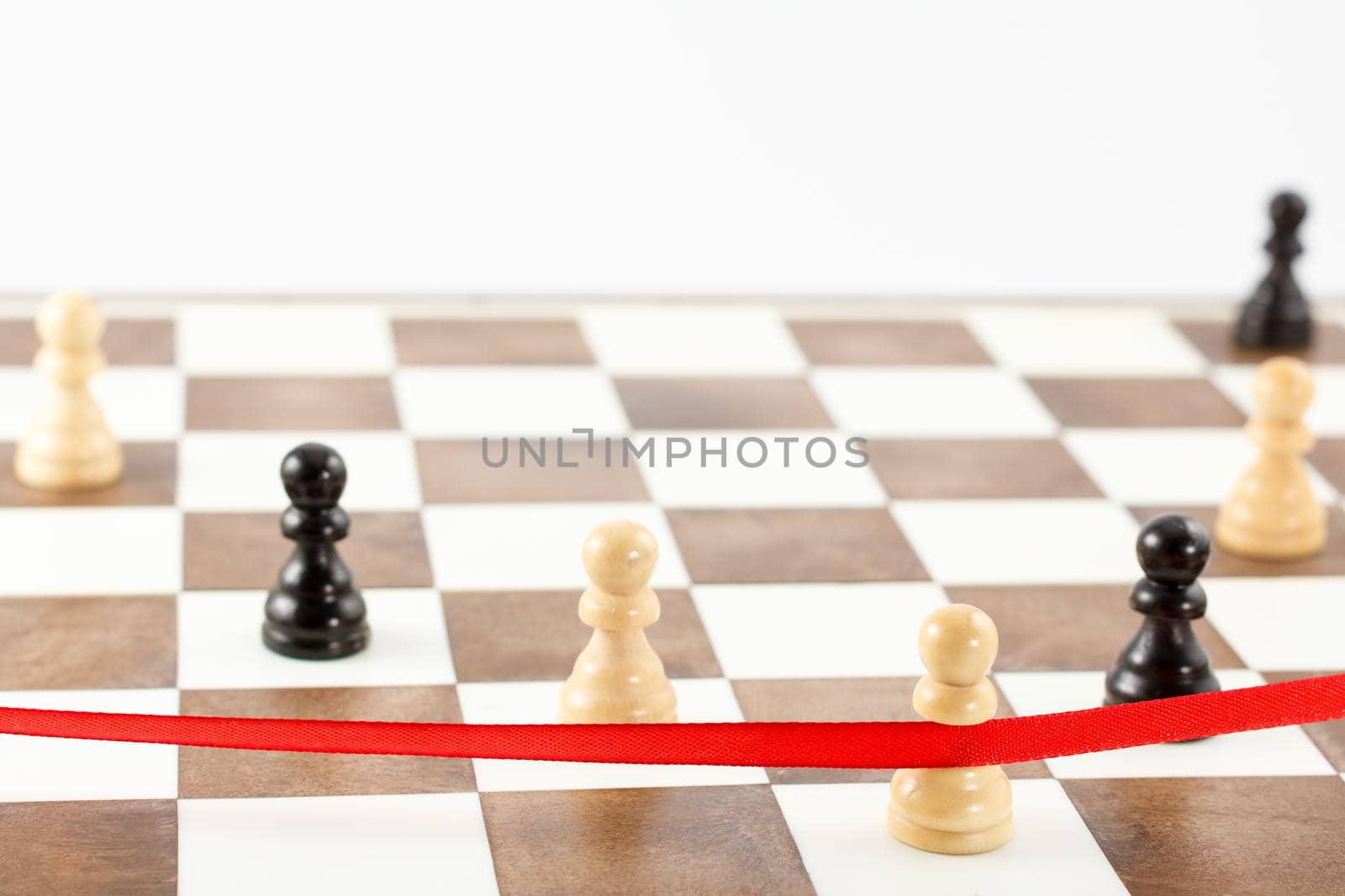 White pawn's figure crossing the red finish ribbon. Chess leadership and success concept