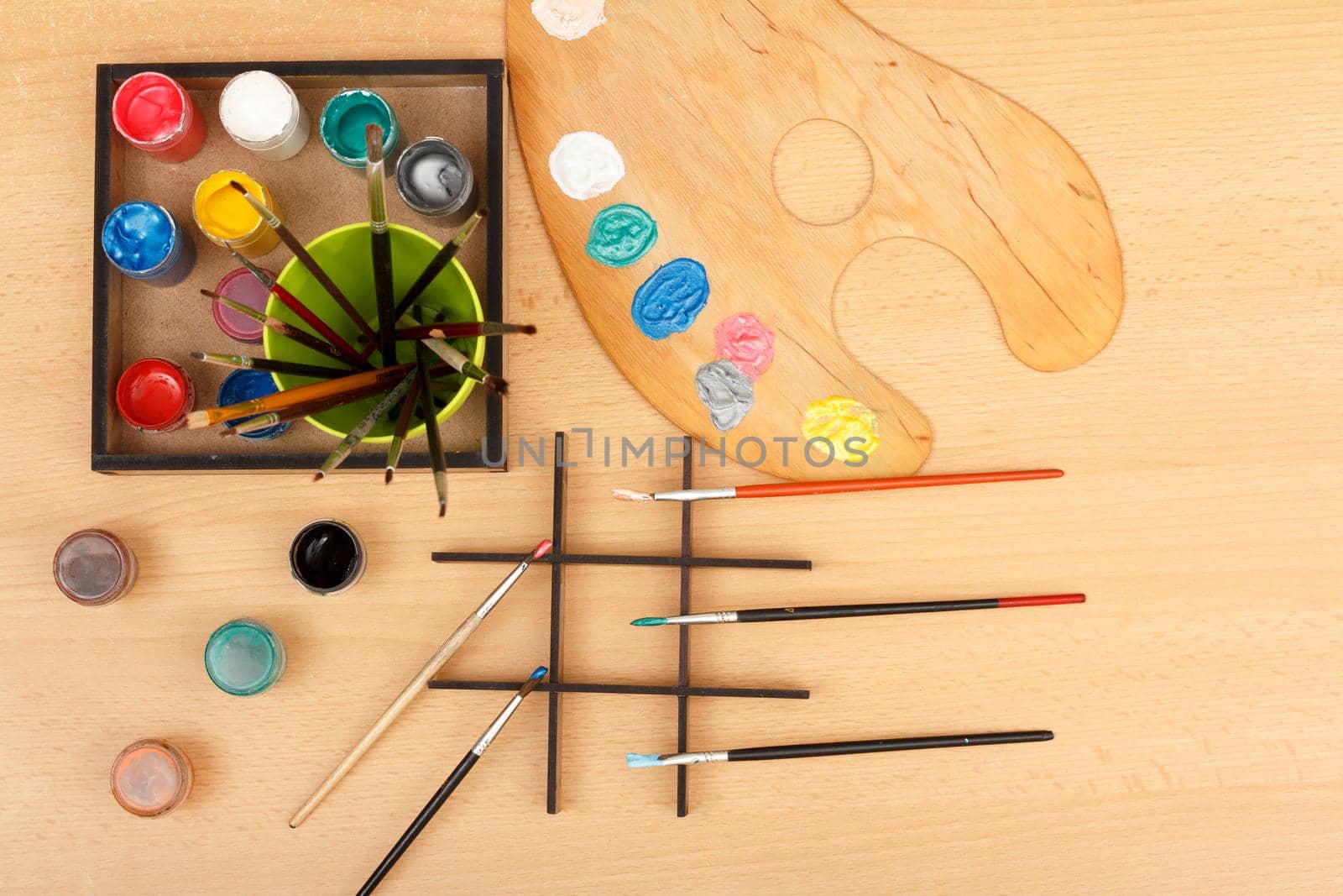 Wooden palette and box with paints and paintbrushes on wooden desk. Top view.