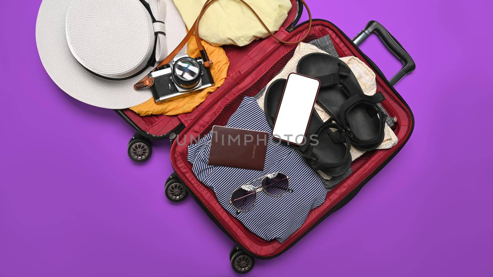 Open suitcase with smart phone, camera, passport and clothes. Preparing for the summer vacations by prathanchorruangsak