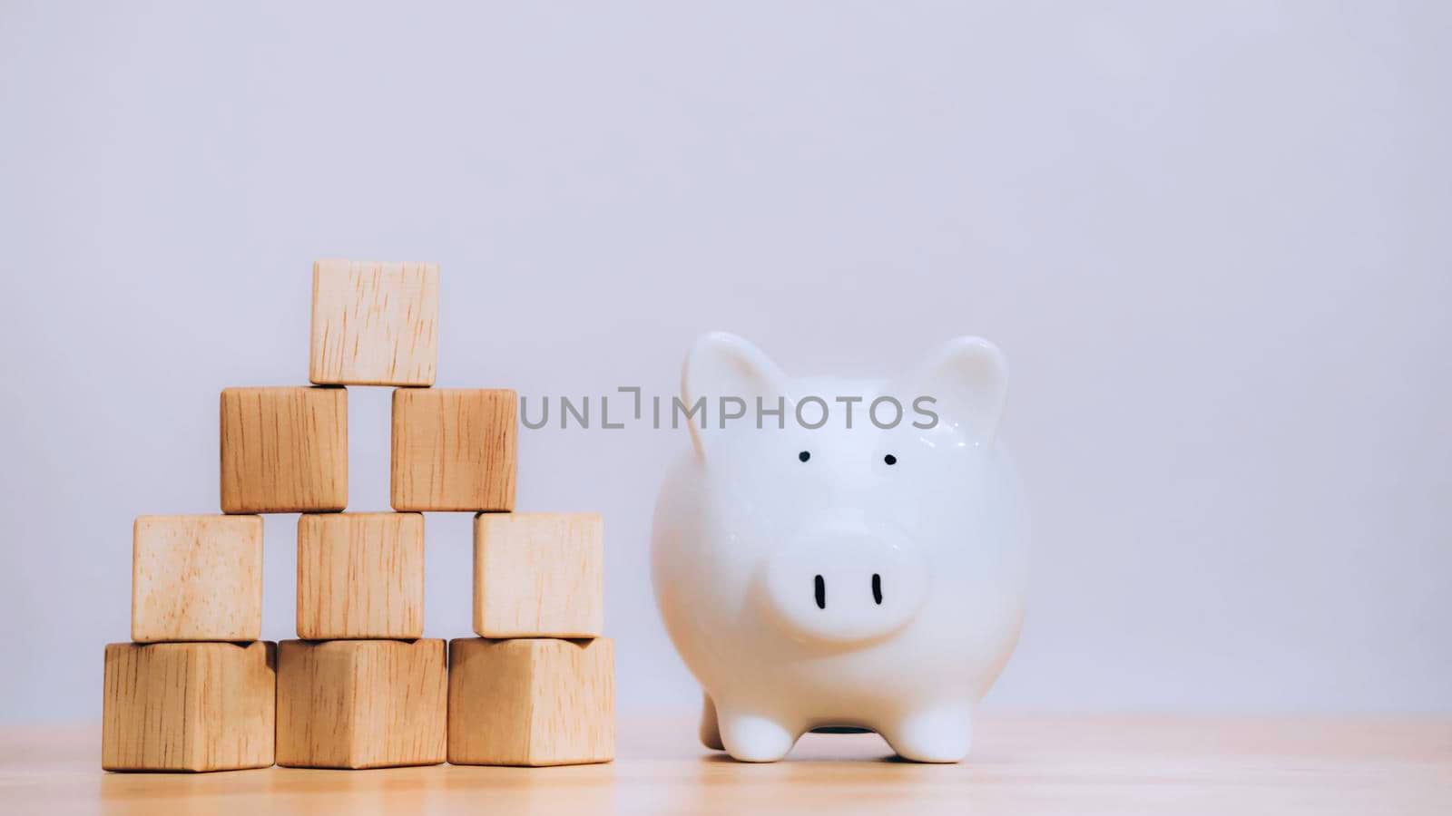 White piggy bank on stack coin near arranging wood cube with arrow symbol stacking as growth step stair on table to security of money invest for future. Growth successful and target concept.