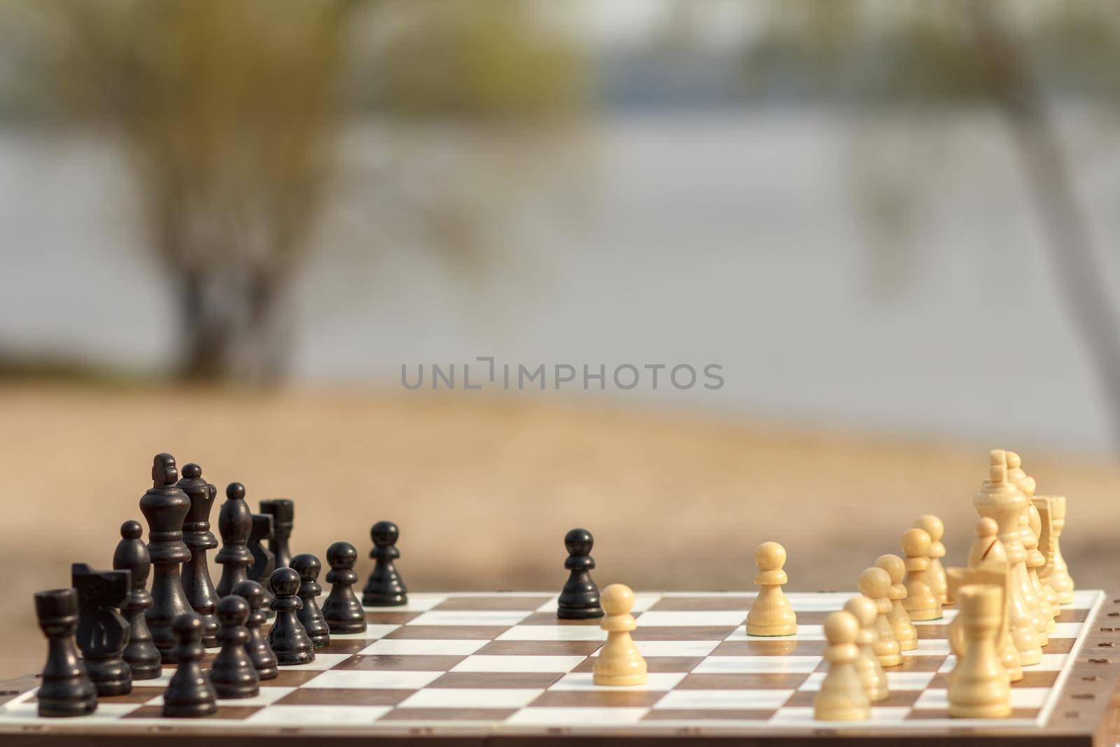 White chess pieces staying against black chess pieces Chess board with chess pieces on wooden bench with river embankment background Selective focus