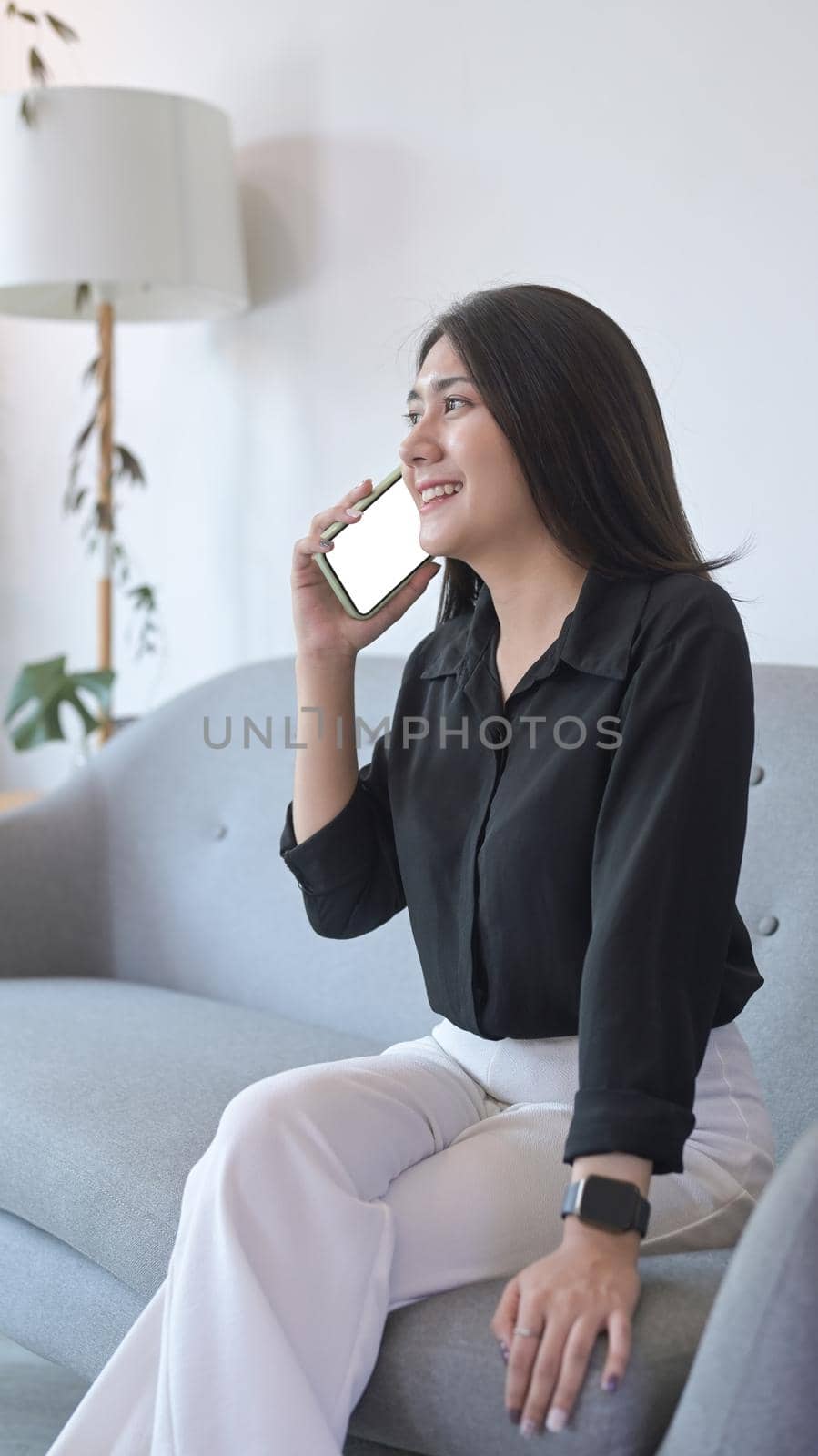 Portrait young woman sitting on couch and having conversation with mobile phone.