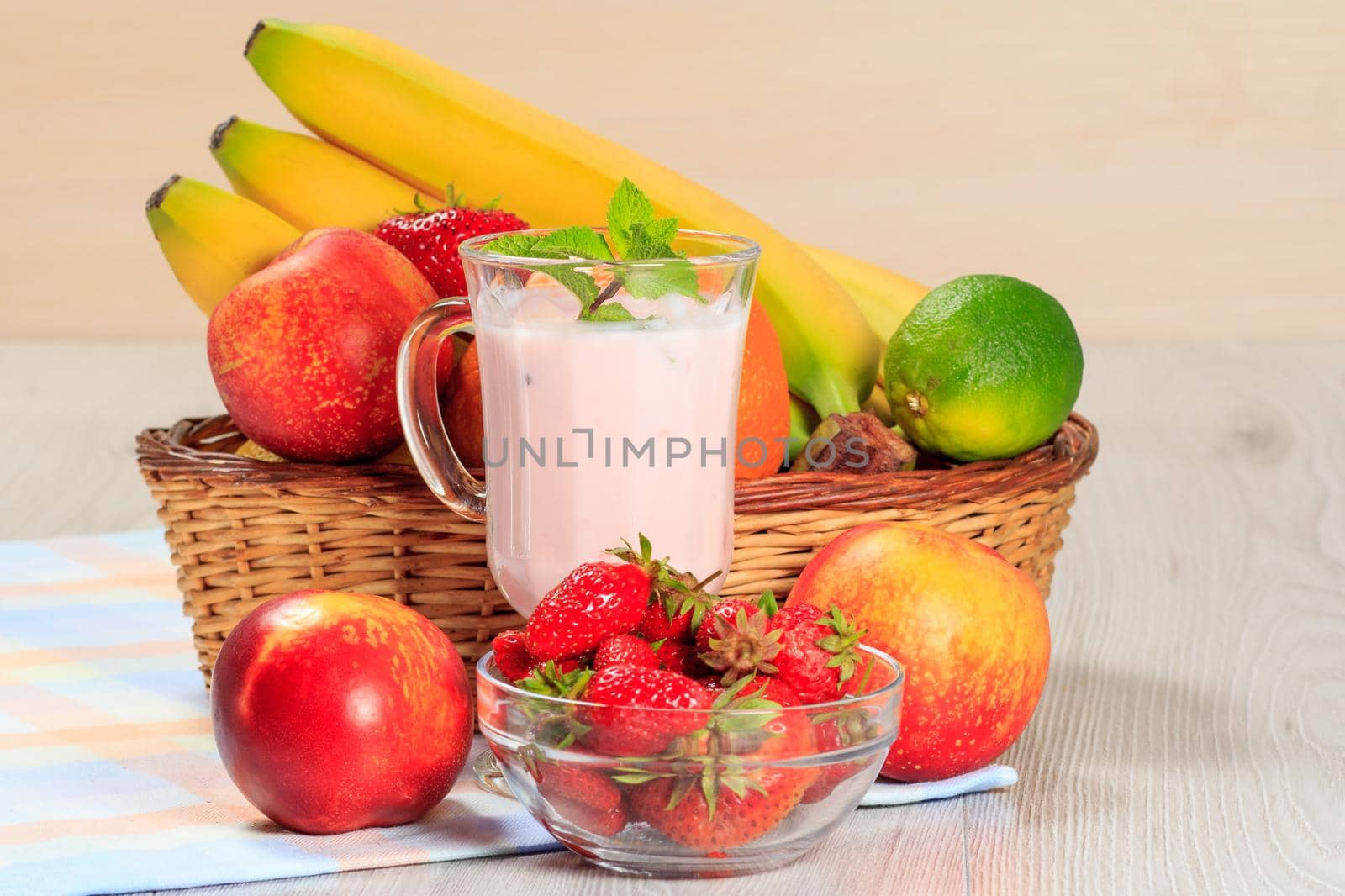 Glass of delicious yogurt with mint and fresh strawberries, banana, lime, nectarine in a wicker basket on a wooden table