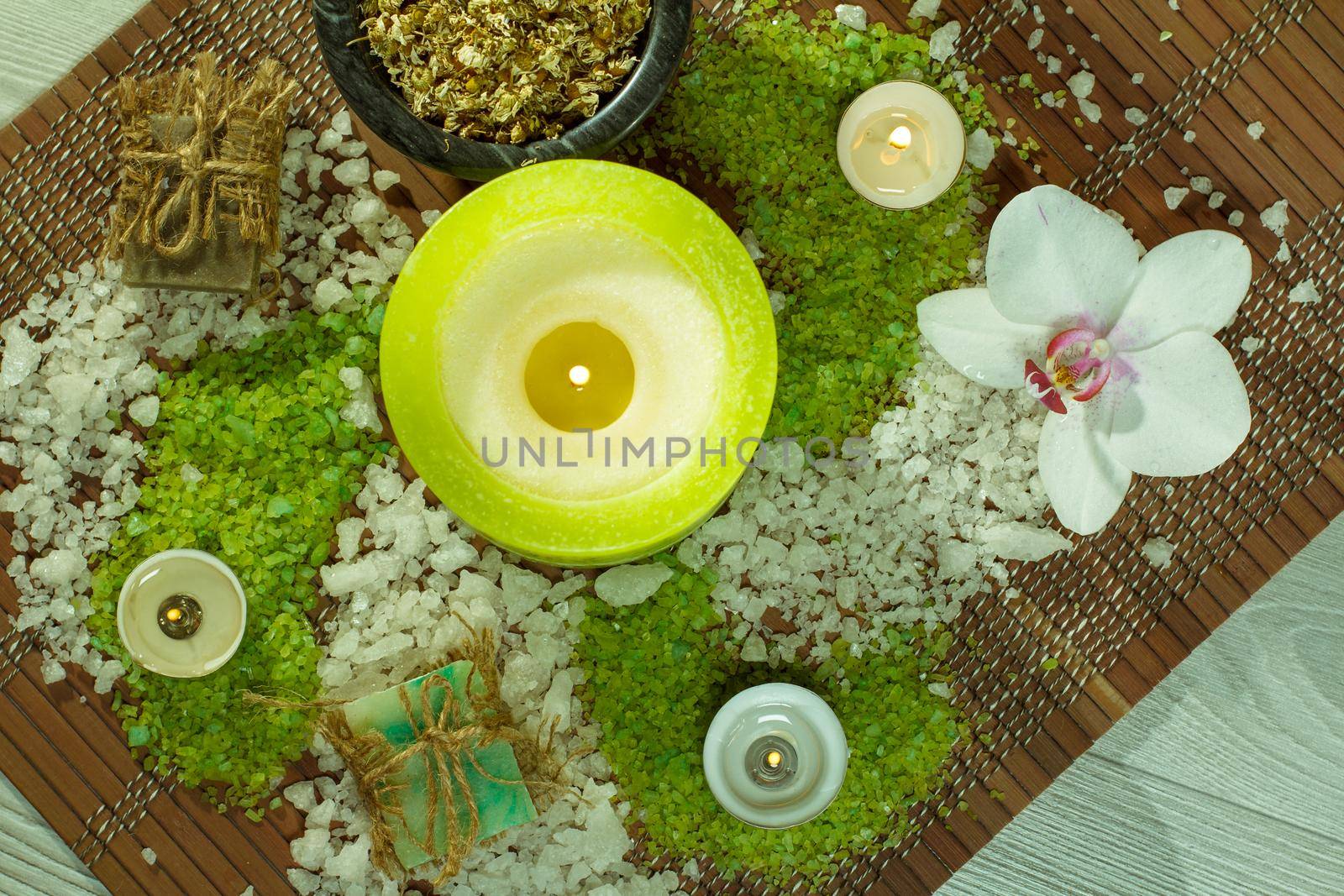 Spa accessories with soap, orchid flower, bowl with dried chamomile flowers, bottles with aromatic oil, sea salt, candles on bamboo napkin