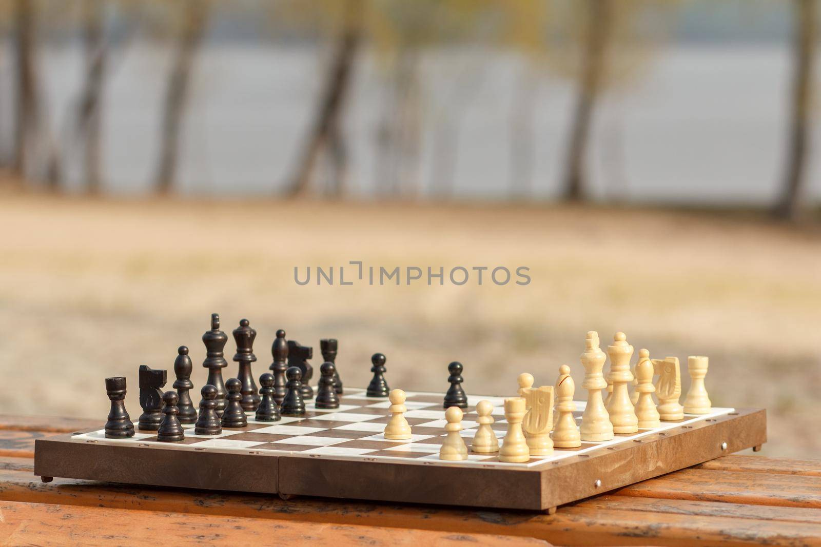 Chess board with chess pieces on wooden bench. Outdoors chess game