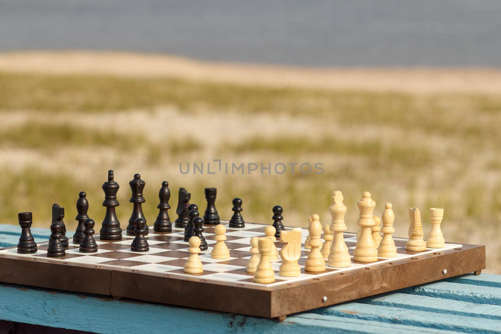 Chess board with chess pieces on wooden bench with river embankment background. Outdoors chess game