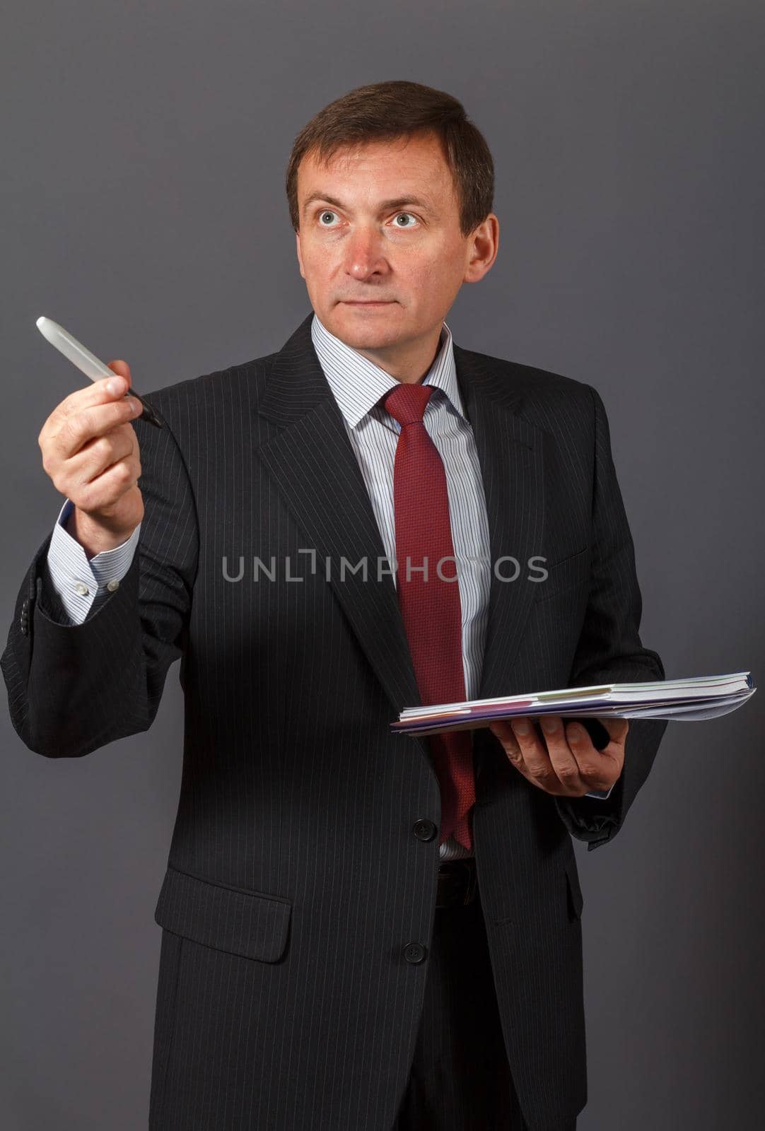 Confident and friendly elegant handsome mature businessman standing in front of a gray background holding a marker and a notebook