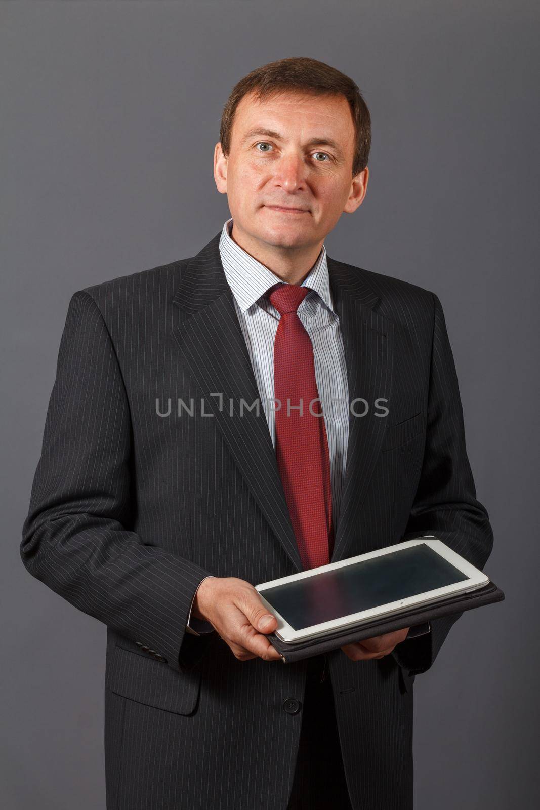 Confident and friendly elegant handsome mature businessman standing in front of a gray background holding a notebook