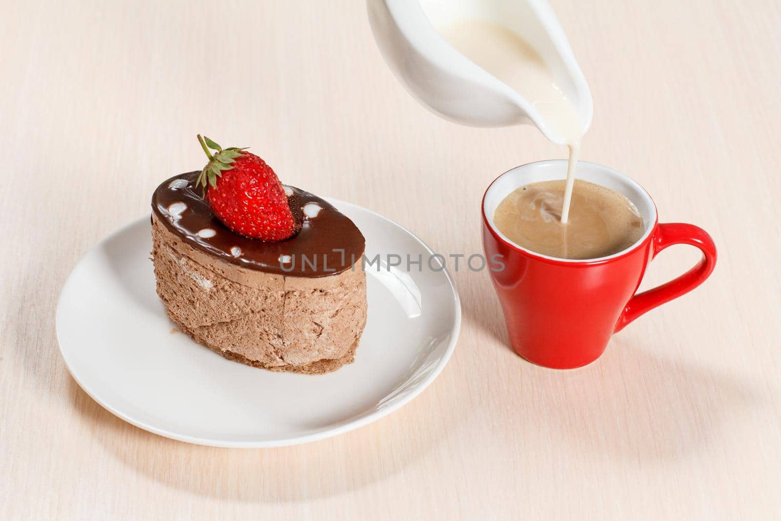 Chocolate cake with strawberry on the white plate, a cup of coffee in which milk is added from a gravy boat