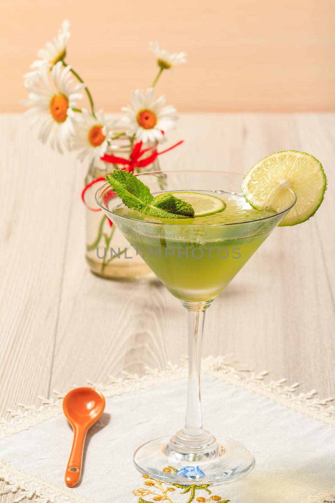 Kiwi jelly with lime pieces in the glass and bouquet of chamomiles on the wooden background