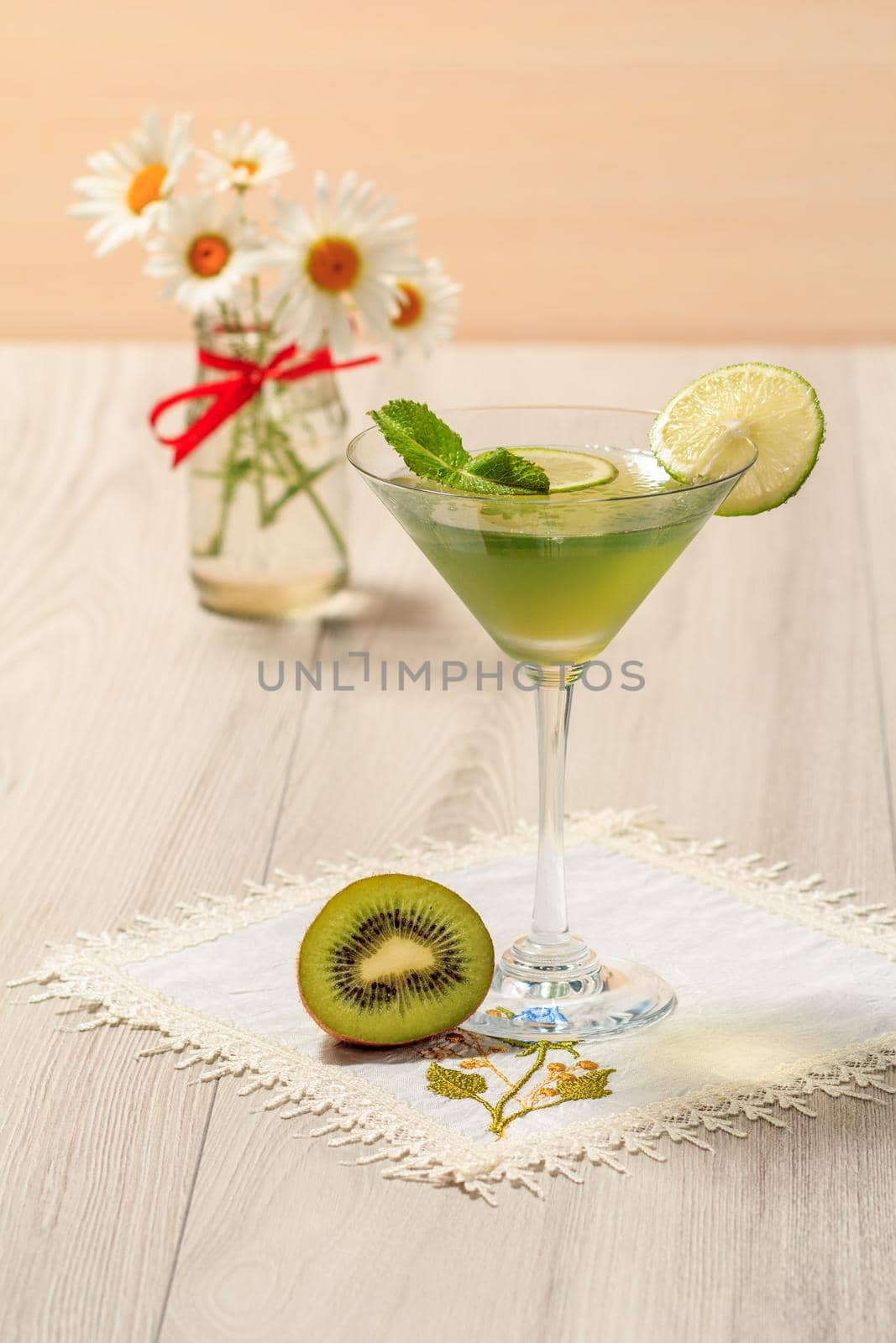 Kiwi jelly with lime pieces in the glass and bouquet of chamomiles on the wooden background