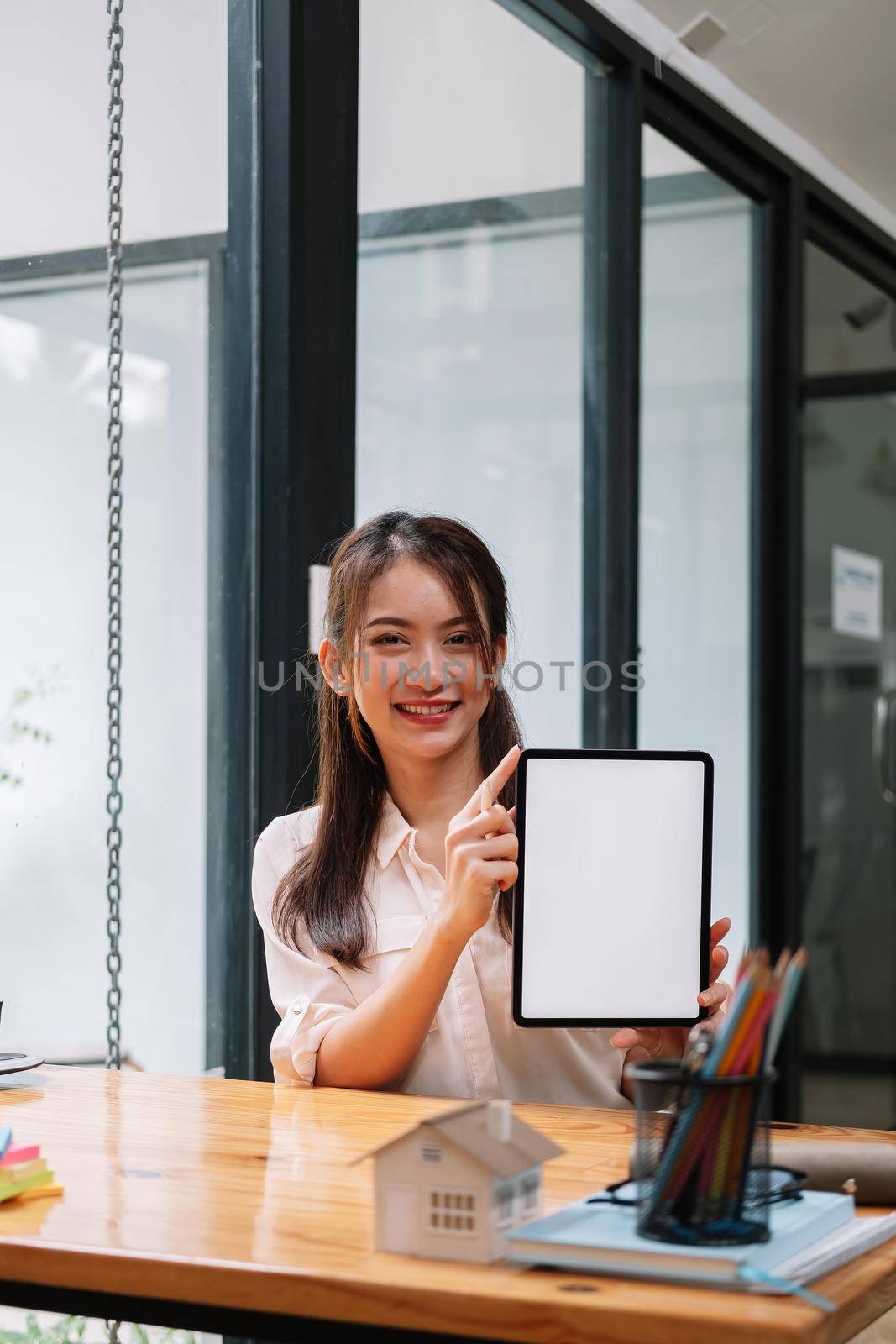 Portrait of Asian woman showing or presenting tablet computer with blank white screen, real estate working at office.