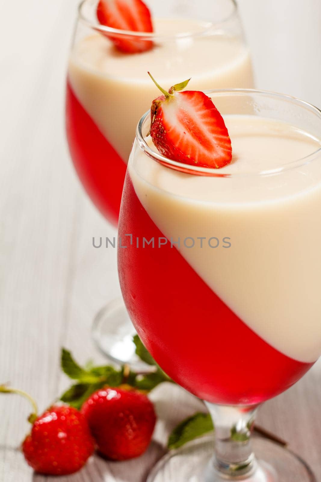 Cherry and milk jelly in the glasses topped strawberry pieces with mint leaves and strawberries on the background