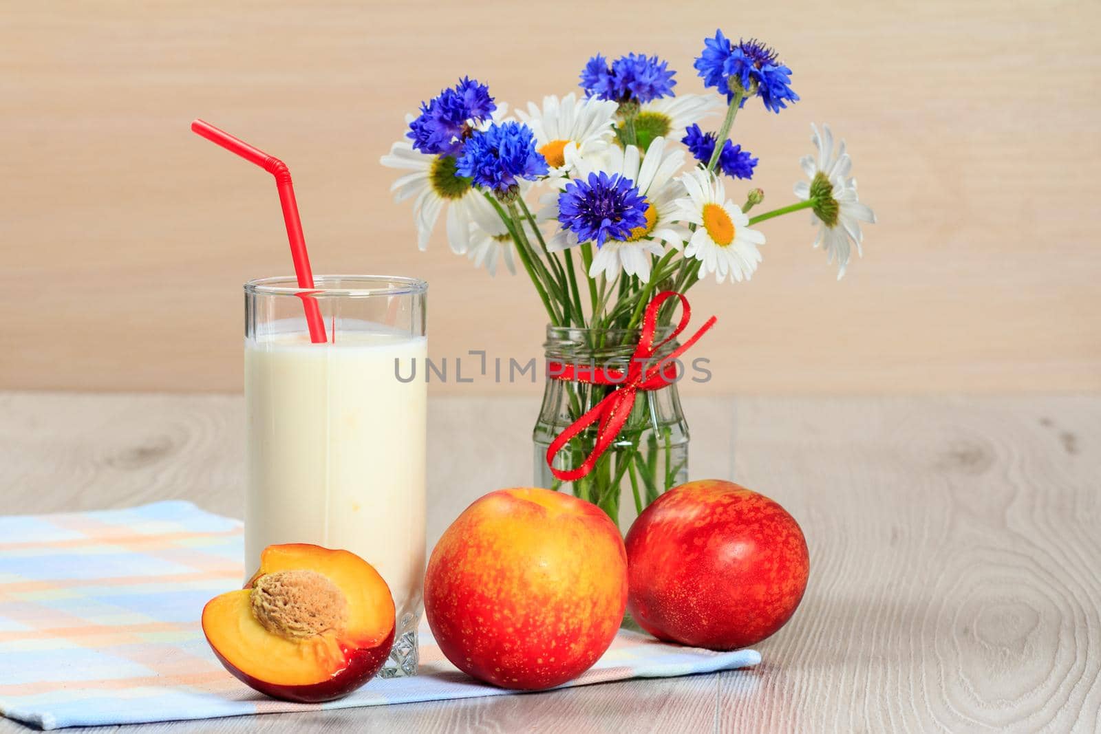 Glass of delicious yogurt with mint and fresh nectarine, chamomile and cornflowers in vase on a wooden table with a napkin