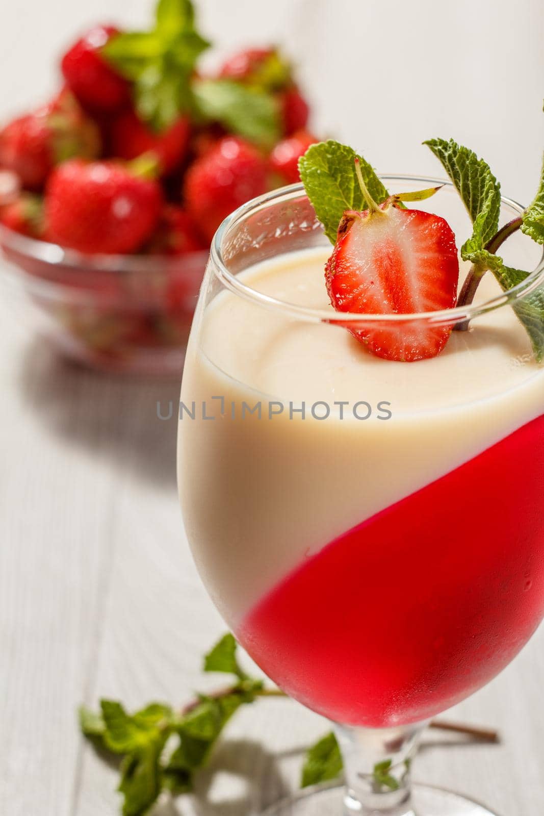 Cherry and milk jelly in the glass topped mint leaves and strawberry piece with strawberries in a bowl on the background