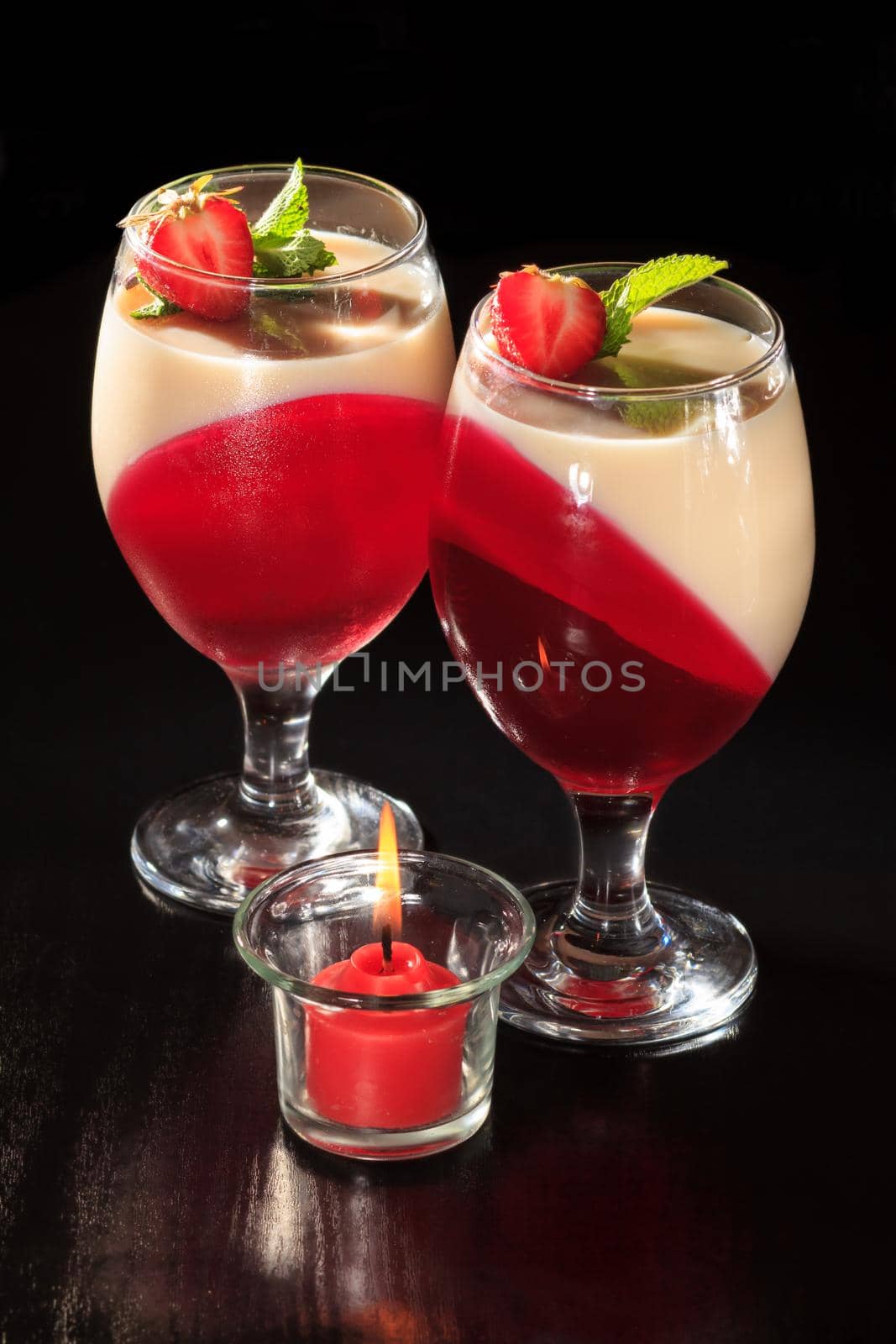 Cherry and milk jelly in the glasses topped mint leaves and strawberry pieces with candle on the black background