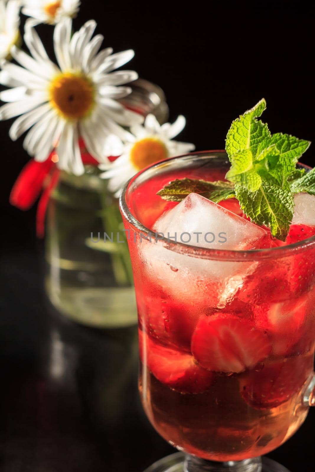 Carbonated lemonade with strawberry slices and mint with flowers of chamomile on the black background. Cold beverage for hot summer day