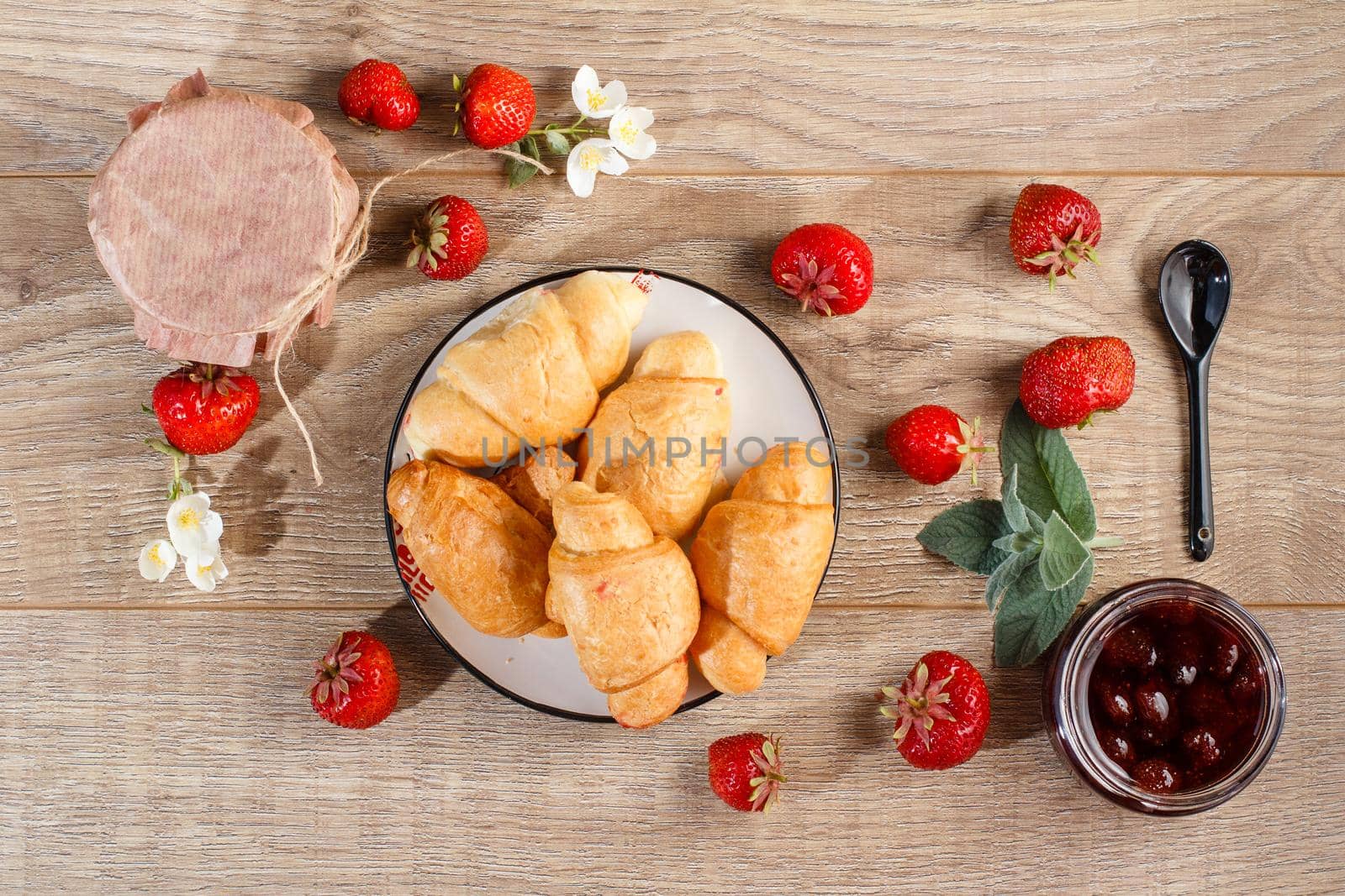 Traditional homemade strawberry jam in jars and plate with croissants, decorated with fresh strawberries Top view