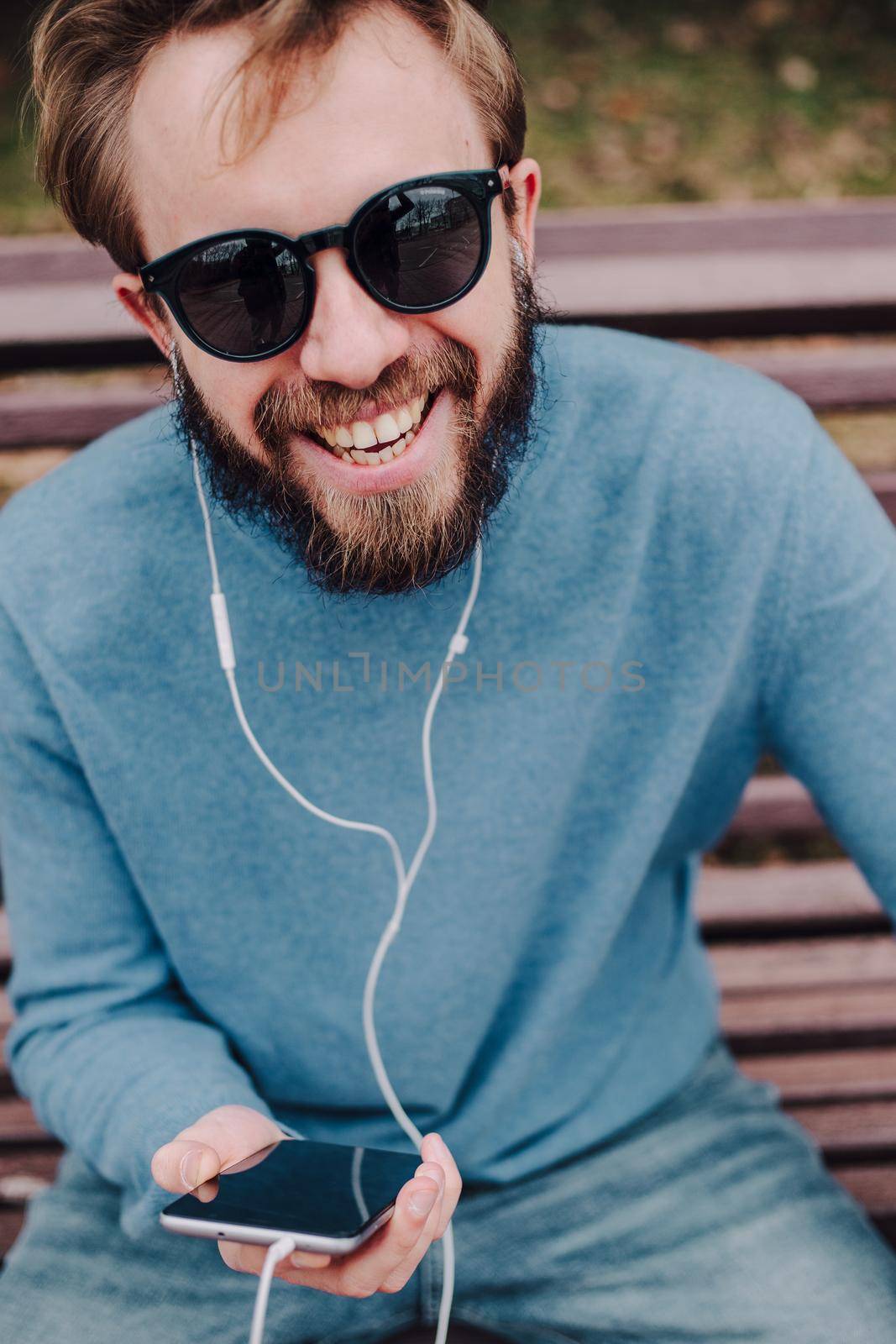 young hipster gay man listening music with headphones siting in a park